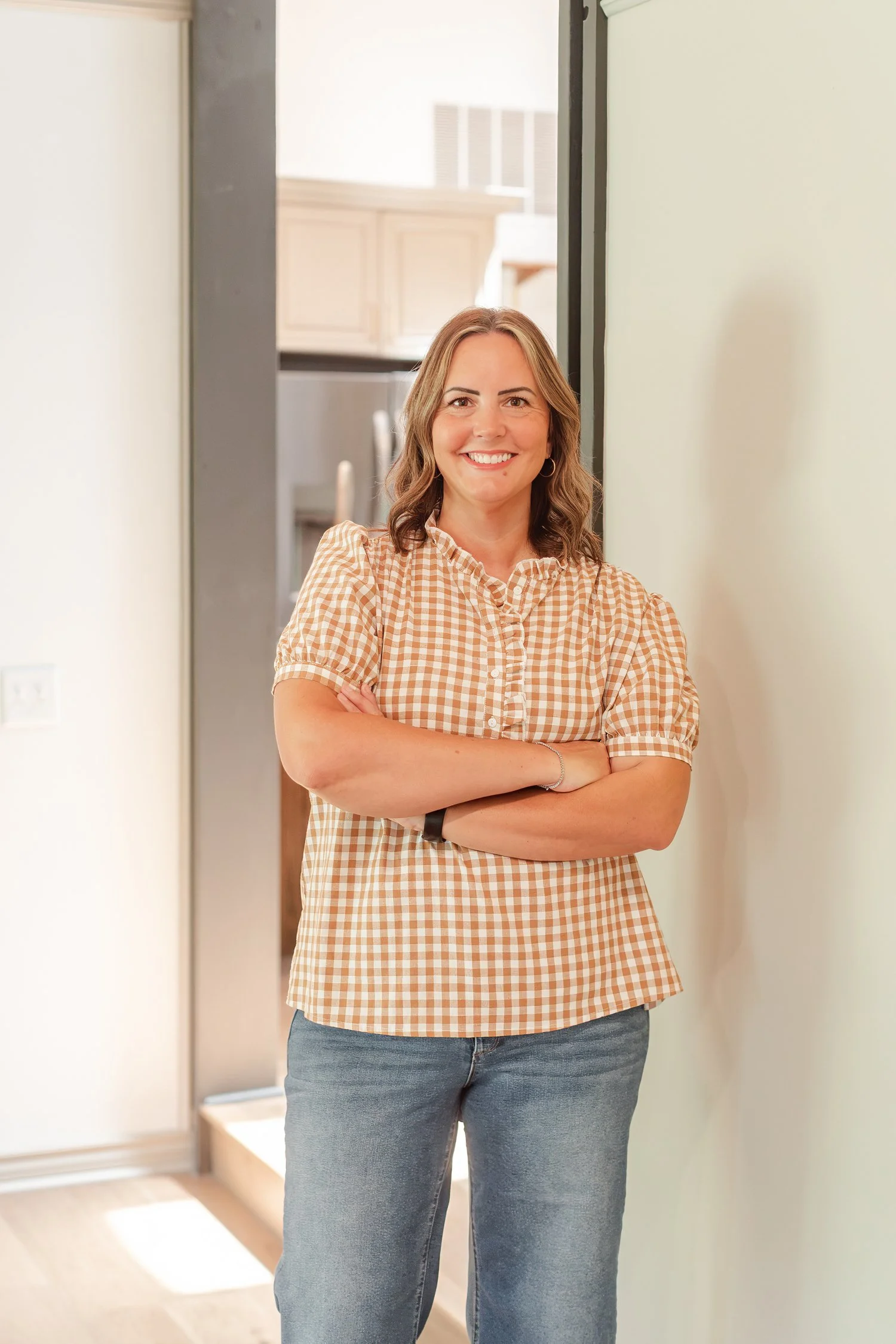 Real estate agent in a tan gingham top with arms crossed in a white doorway, team headshots in Bolivar, MO