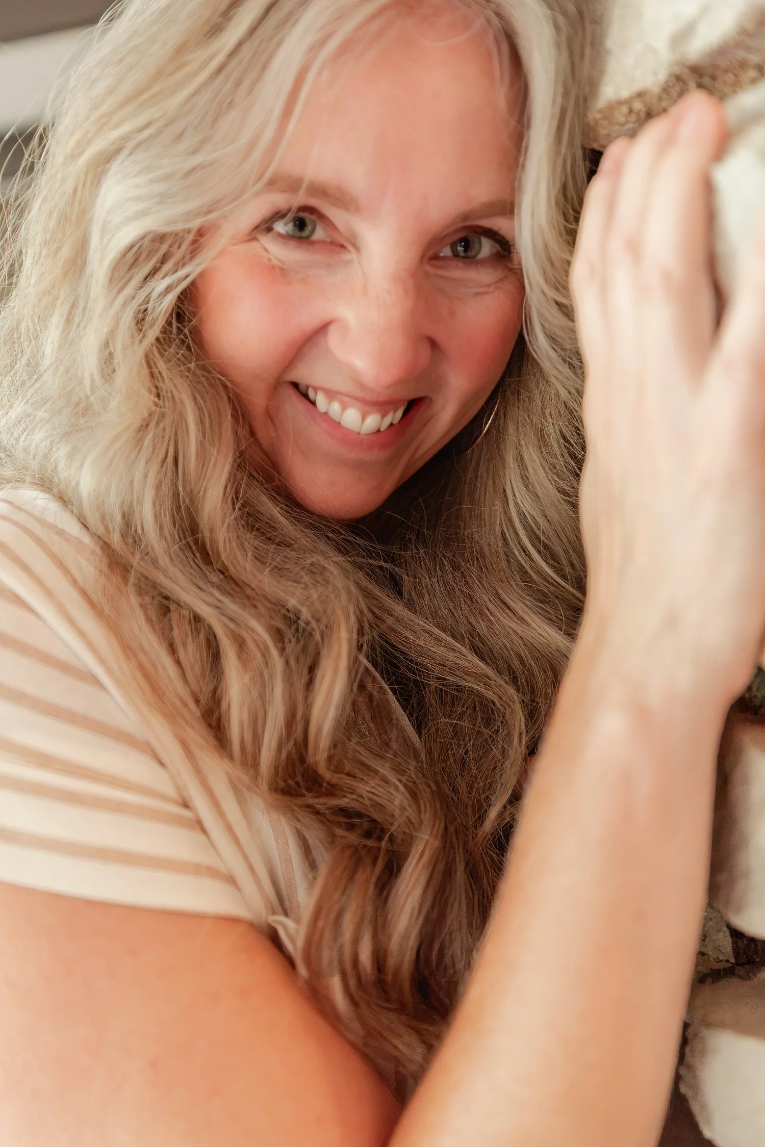 Close up of a smiling real estate agent with long wavy hair resting a hand on a stone wall, headshot in Bolivar, MO