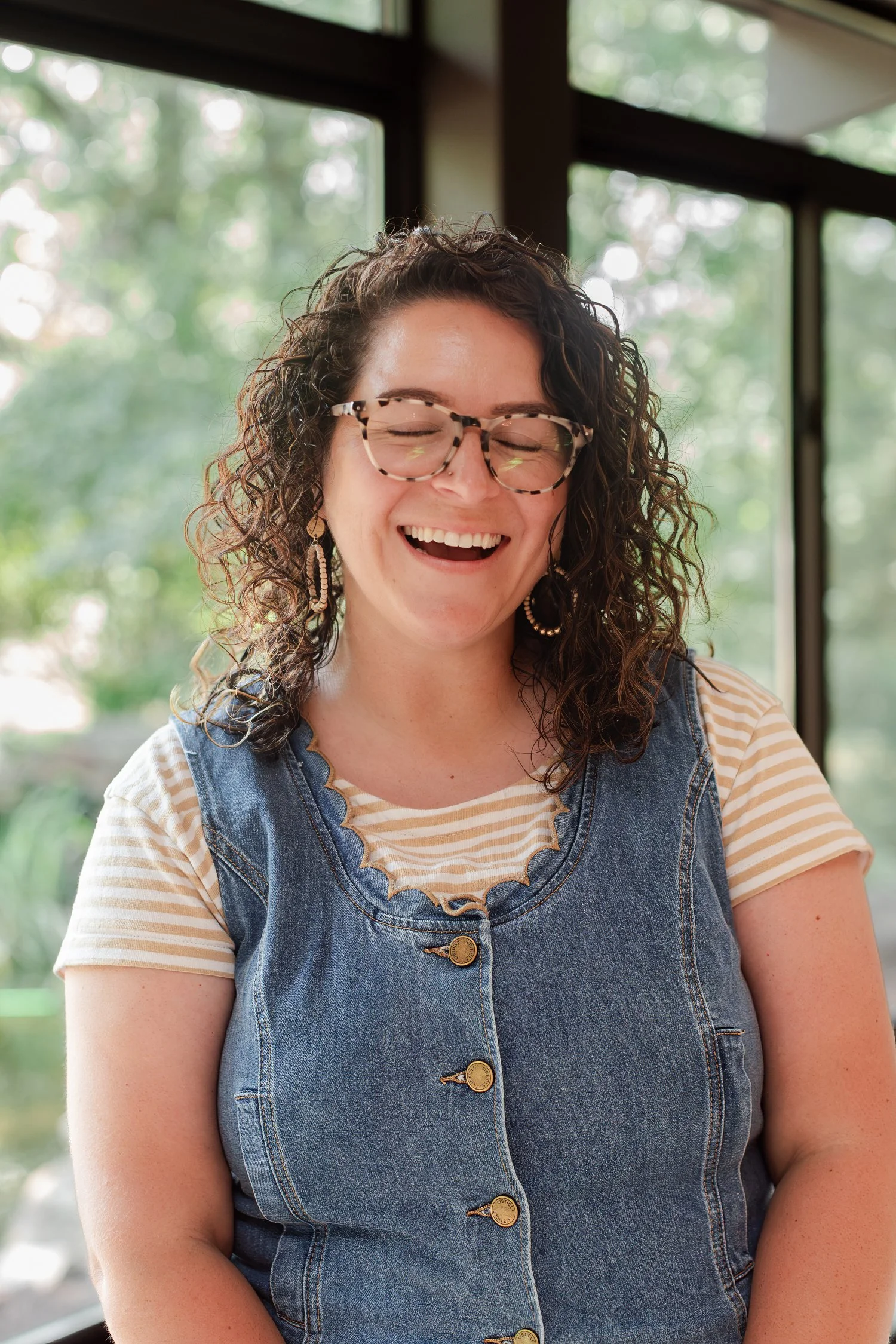Real estate agent in glasses and a denim vest laughing by a wall of windows, Stellar Real Estate Co. team photos in Bolivar, MO