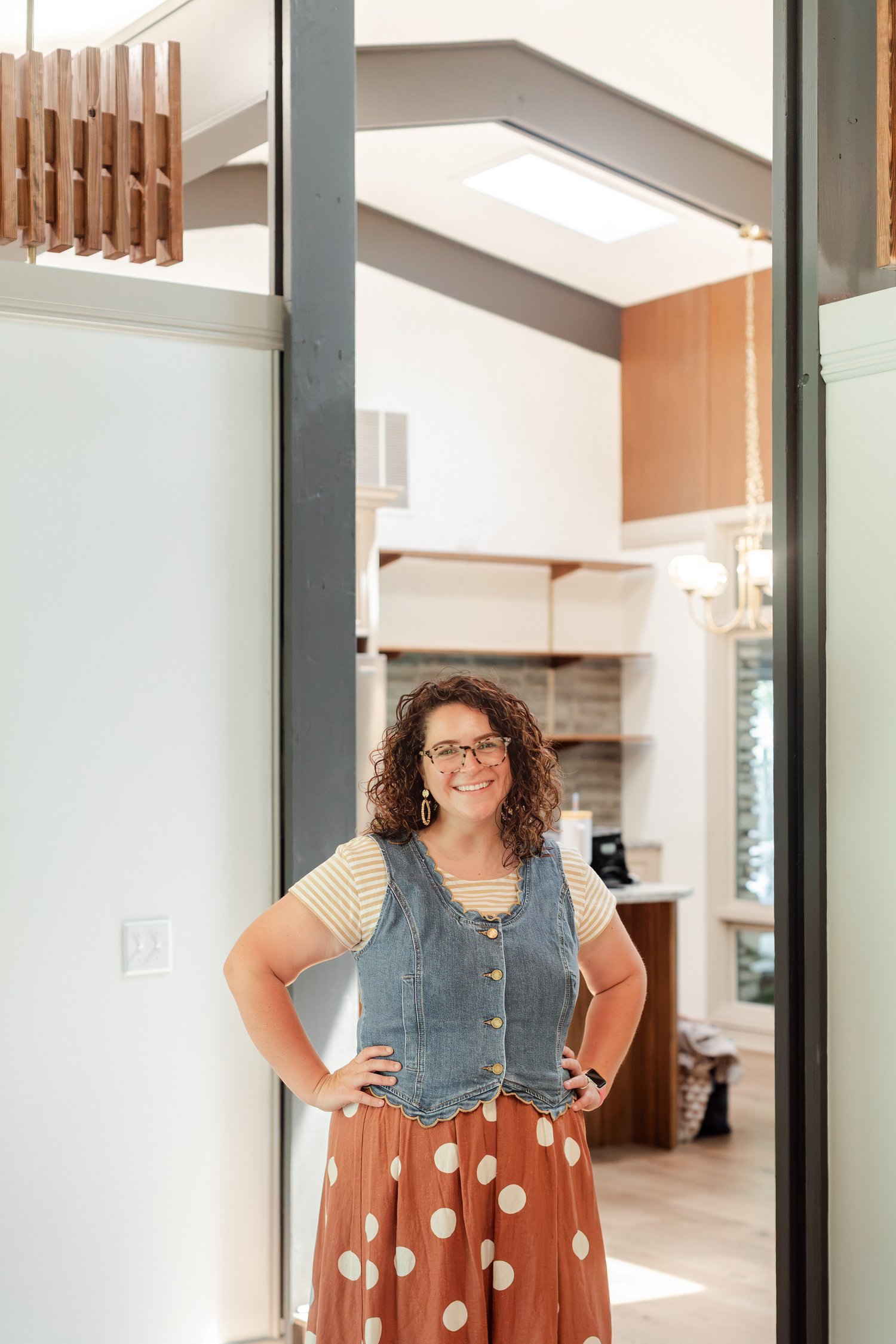 Real estate agent in a denim vest and rust polka dot skirt standing in a hallway with hands on hips, full length photo in Bolivar, MO