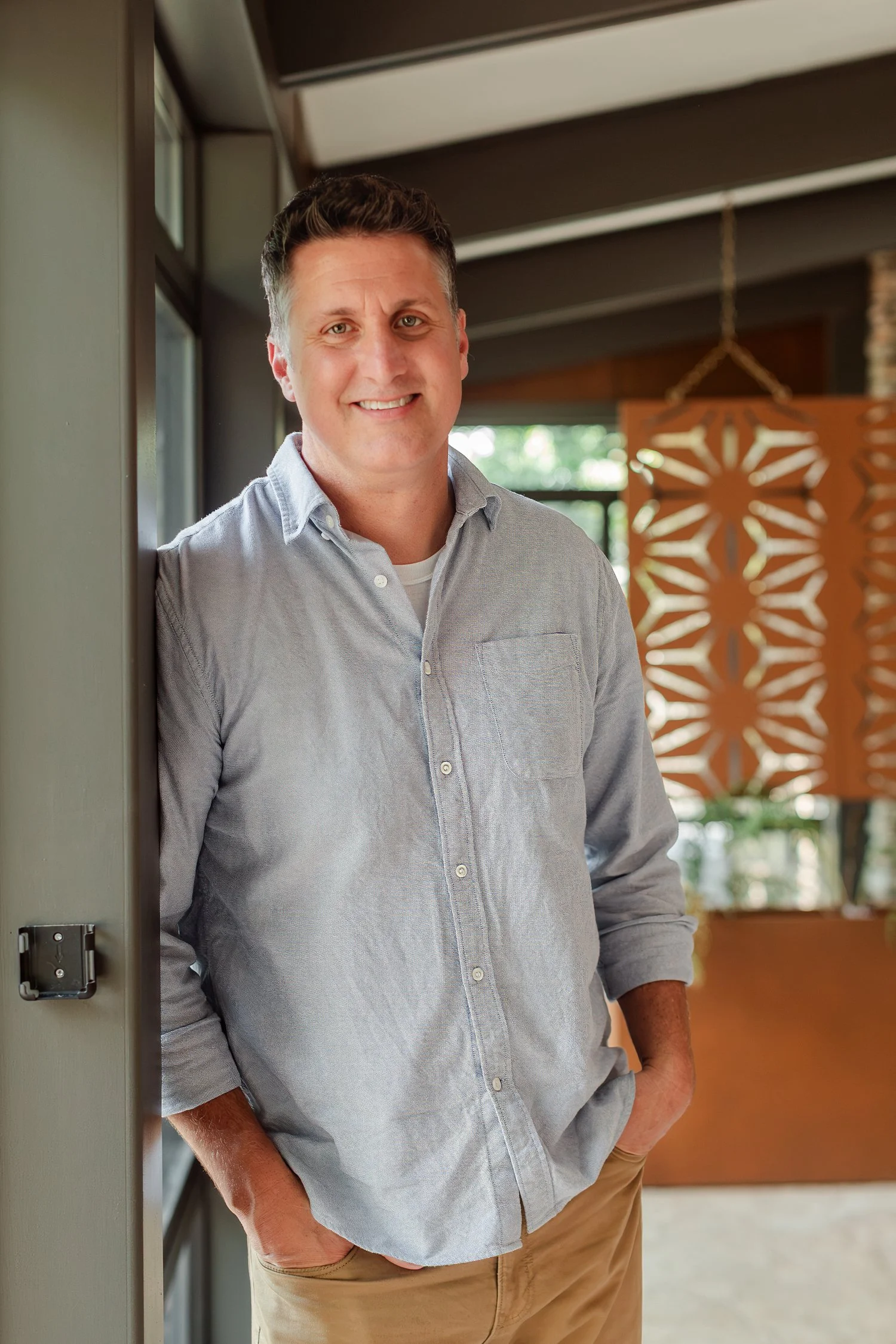 Real estate agent in a chambray shirt leaning in a doorway beside a rust metal screen, real estate agent headshots in Bolivar, MO