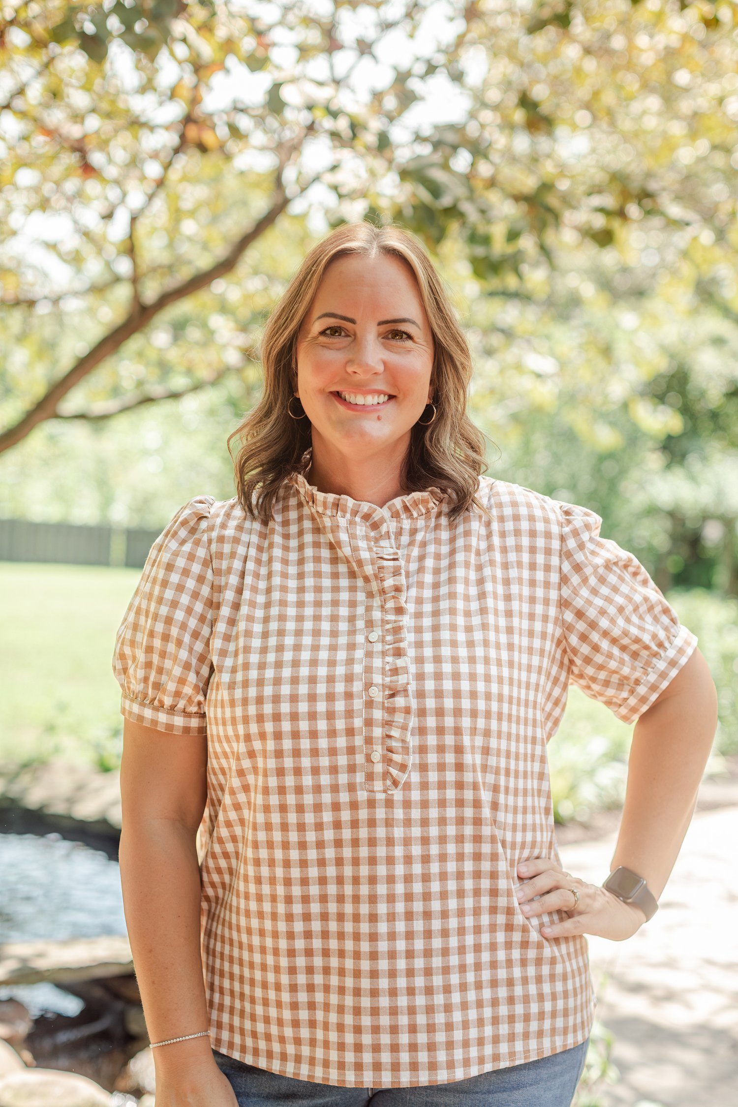 Real estate agent in a tan gingham top standing in the garden under the trees, realtor headshots in Bolivar, MO