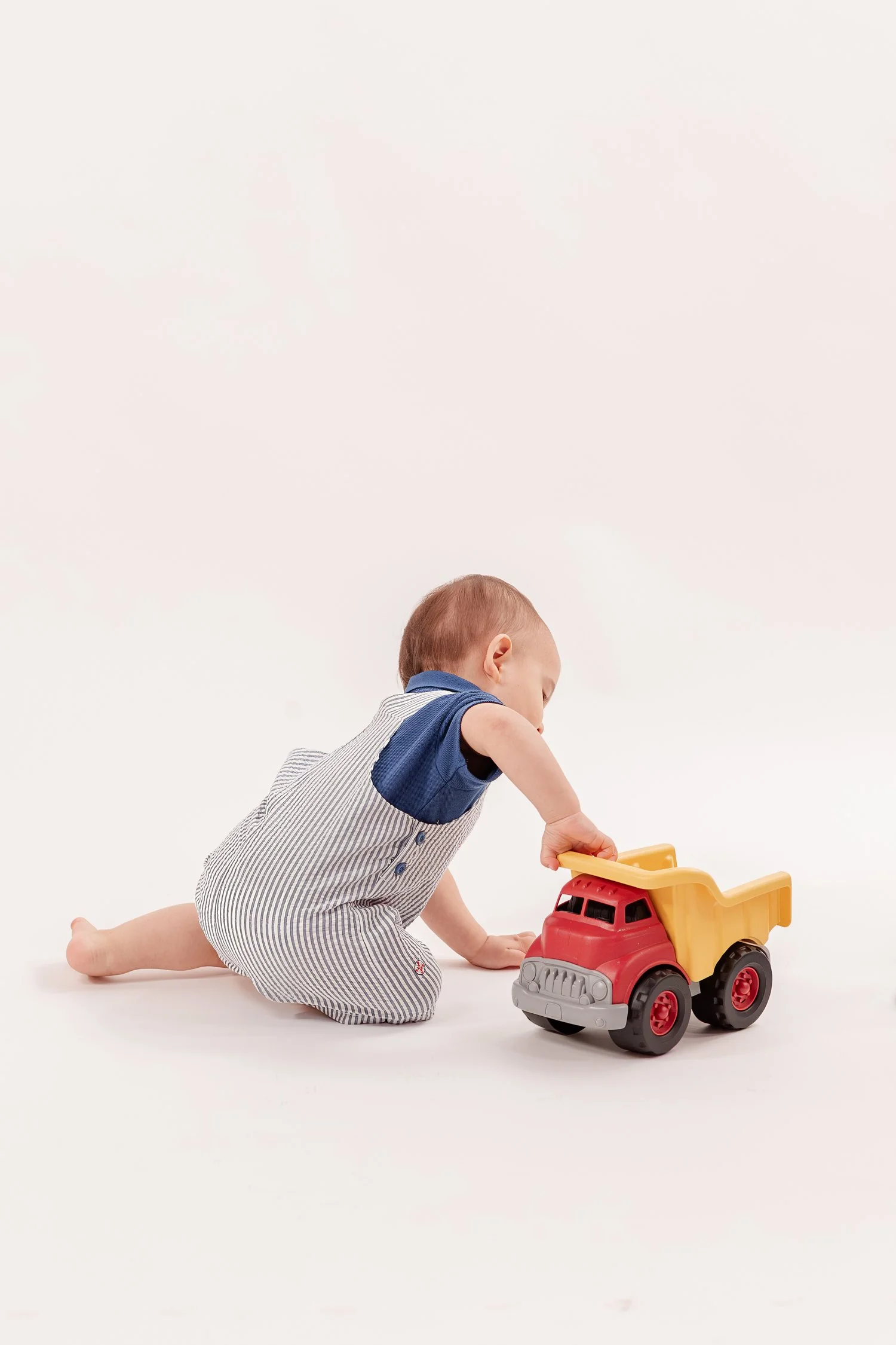 Winston sitting on the floor and reaching toward a toy dump truck