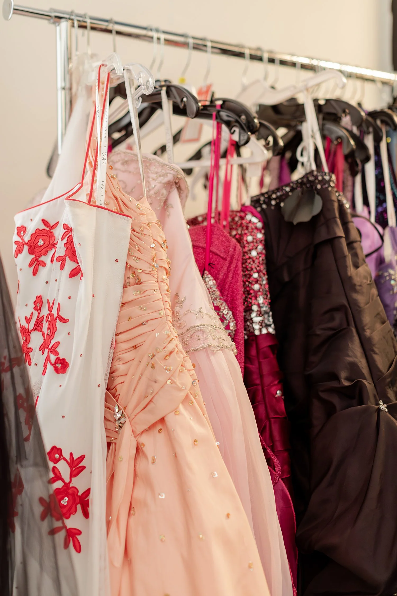 Rack of prom gowns in white, peach, pink, and magenta, brand photos for H&H New Creations Boutique in Bolivar MO