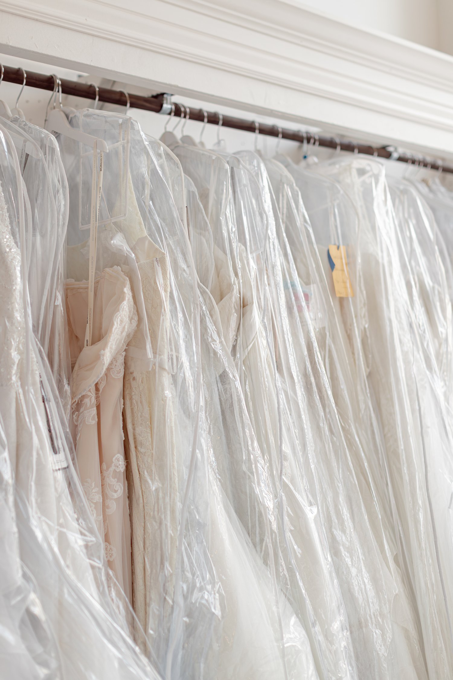 White and ivory gowns in clear bags on a wall rack, brand photos for H&H New Creations Boutique in Bolivar MO