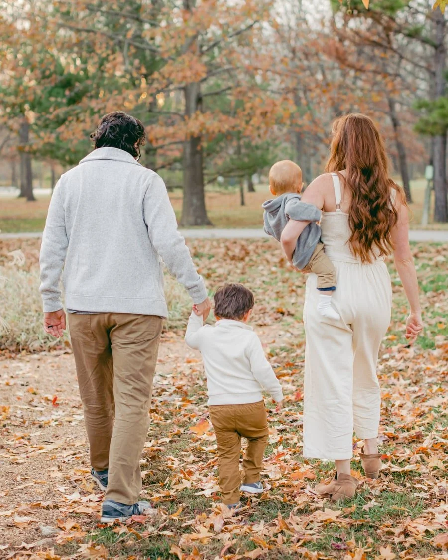 Family seen from behind walking together through fallen leaves.