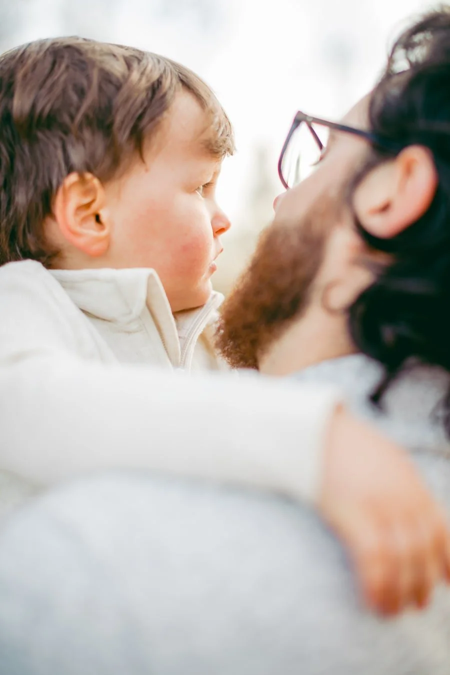 Close view of a child in a cream sweater held against his father’s shoulder.