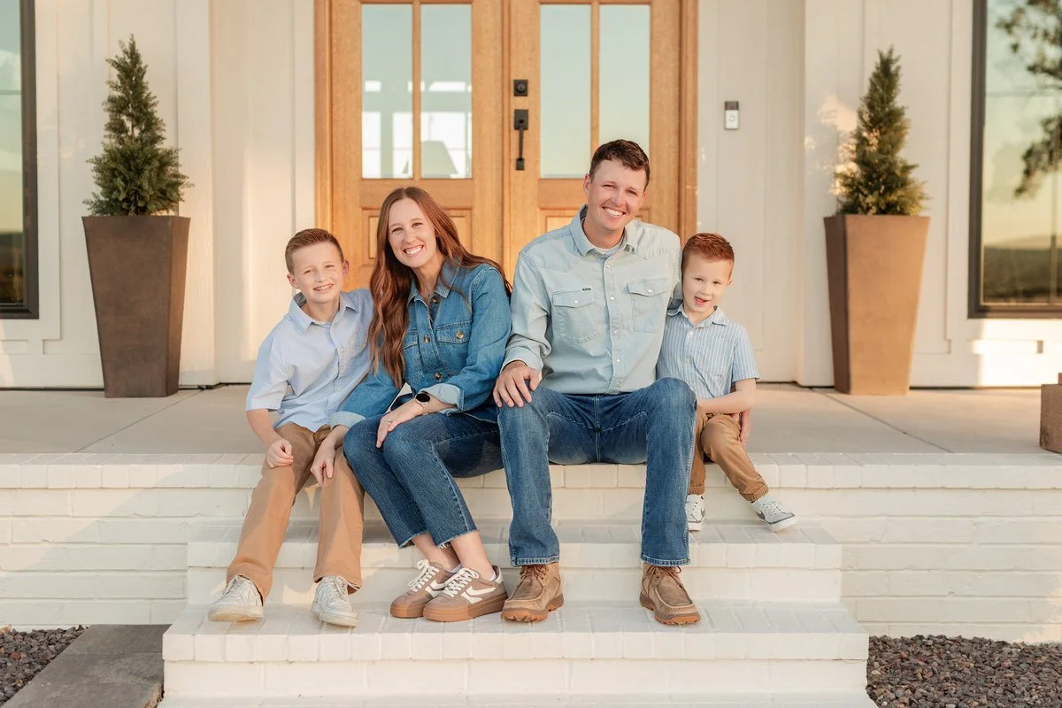 Family of four in blue denim shirts, jeans, and tan pants sitting on front steps.