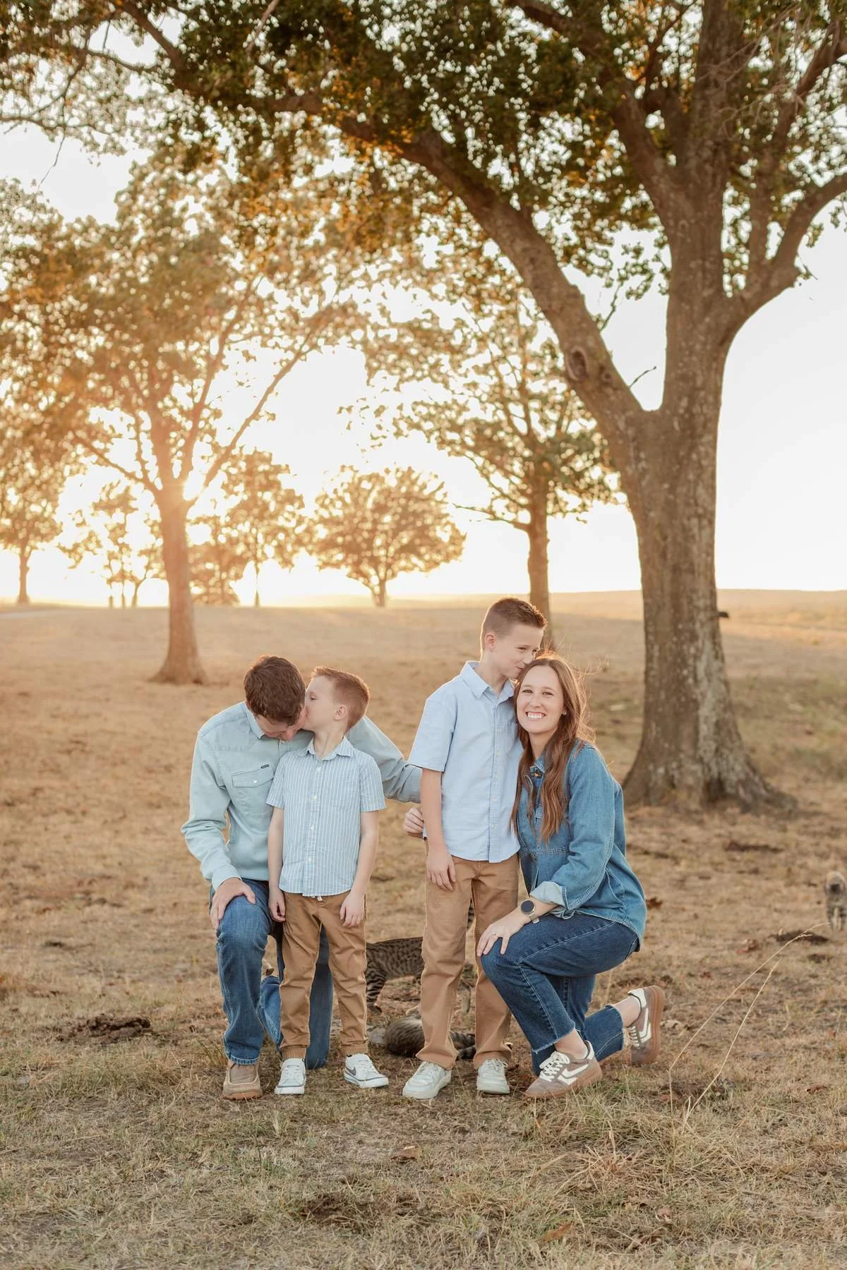 Family of four wearing blue and tan beneath trees in fall.