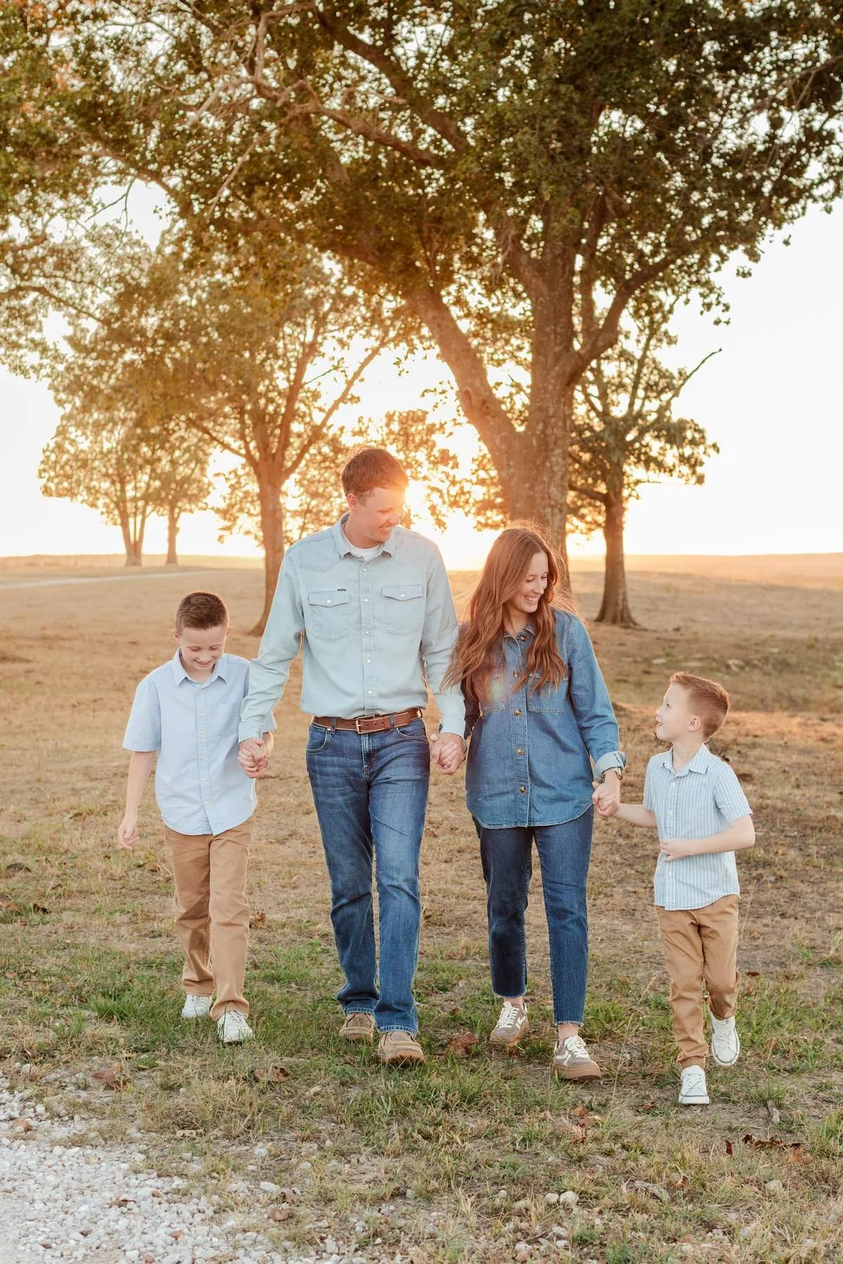 Family holding hands outdoors in blue shirts, jeans, and tan pants.