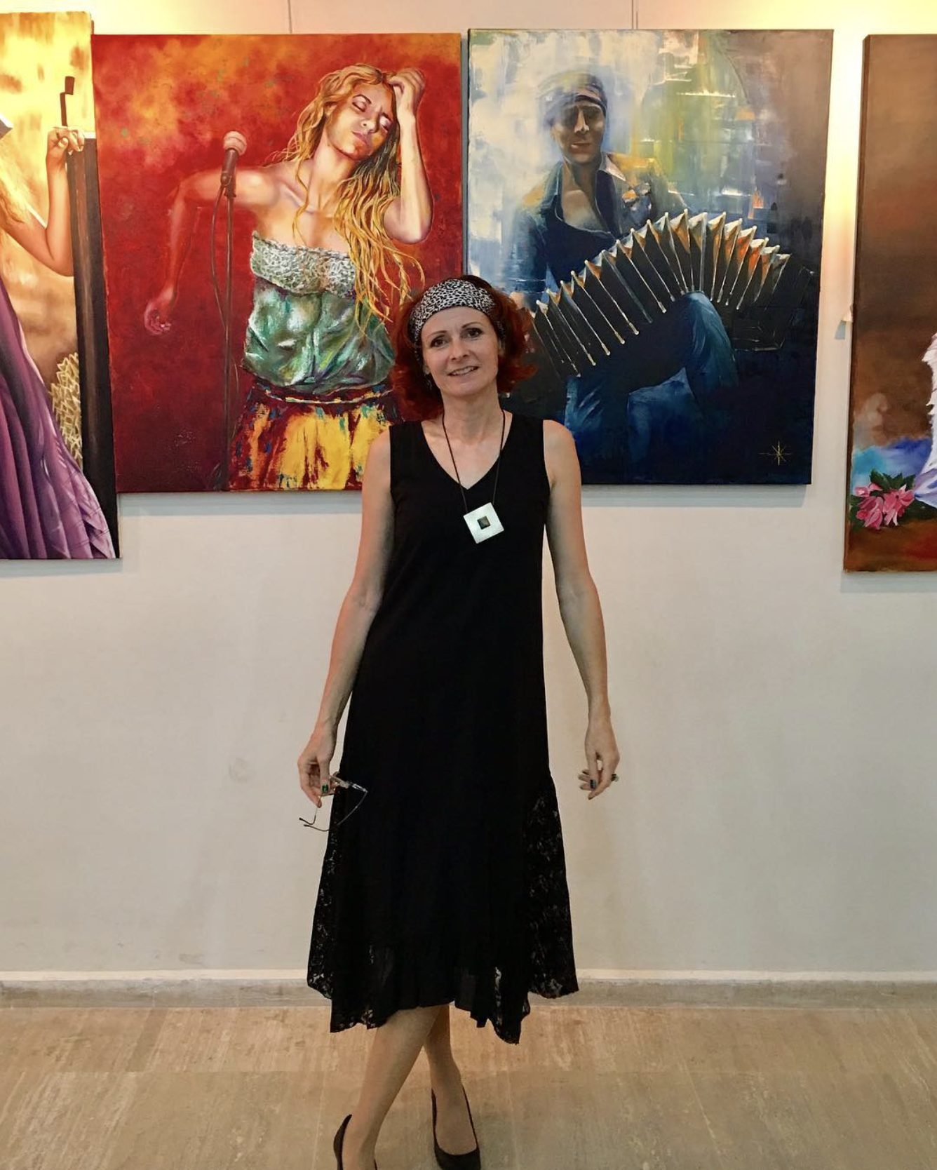 Eine Frau in einem schwarzen Kleid vor farbenfrohen Gemälden in einer Galerie.
