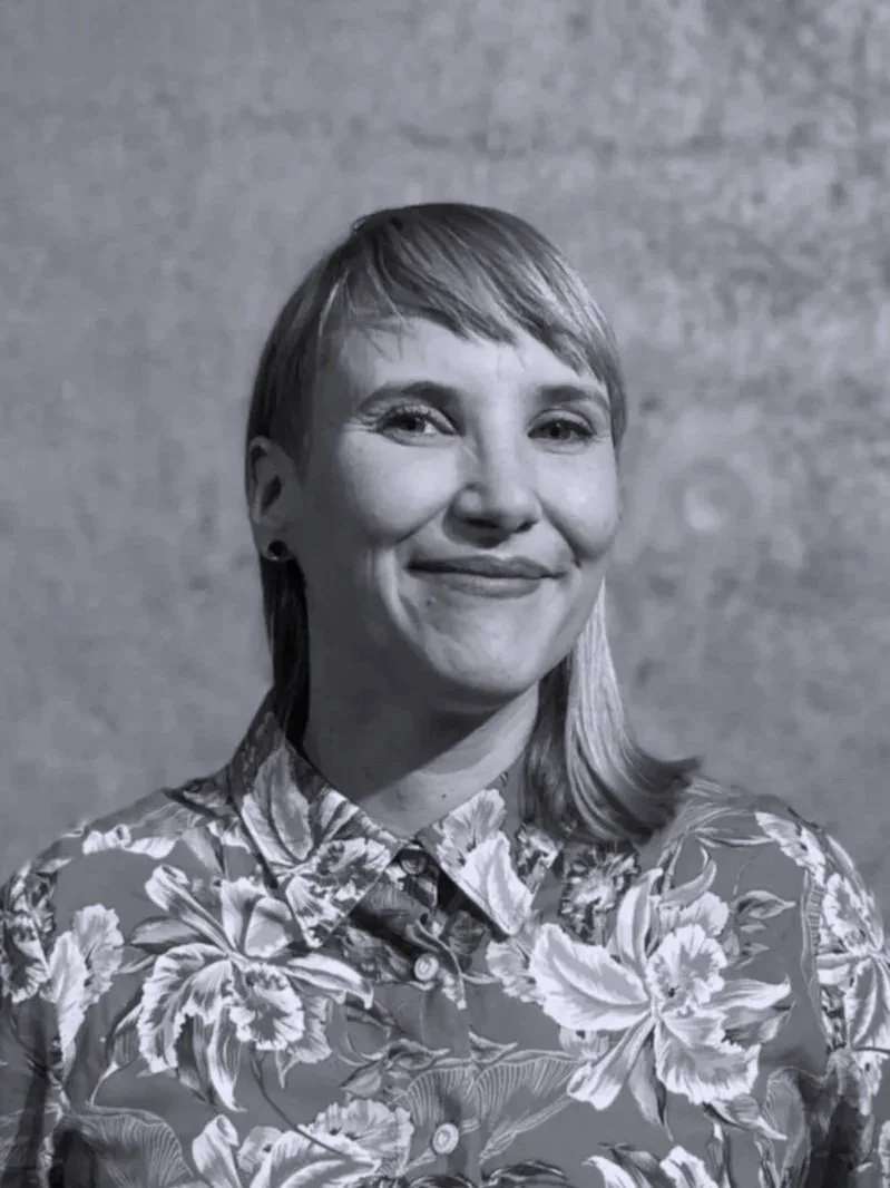 Mustavalkoinen valokuva Virvestä, joka hymyilee veikeästi kameralle. Virvellä on kukkapaita.