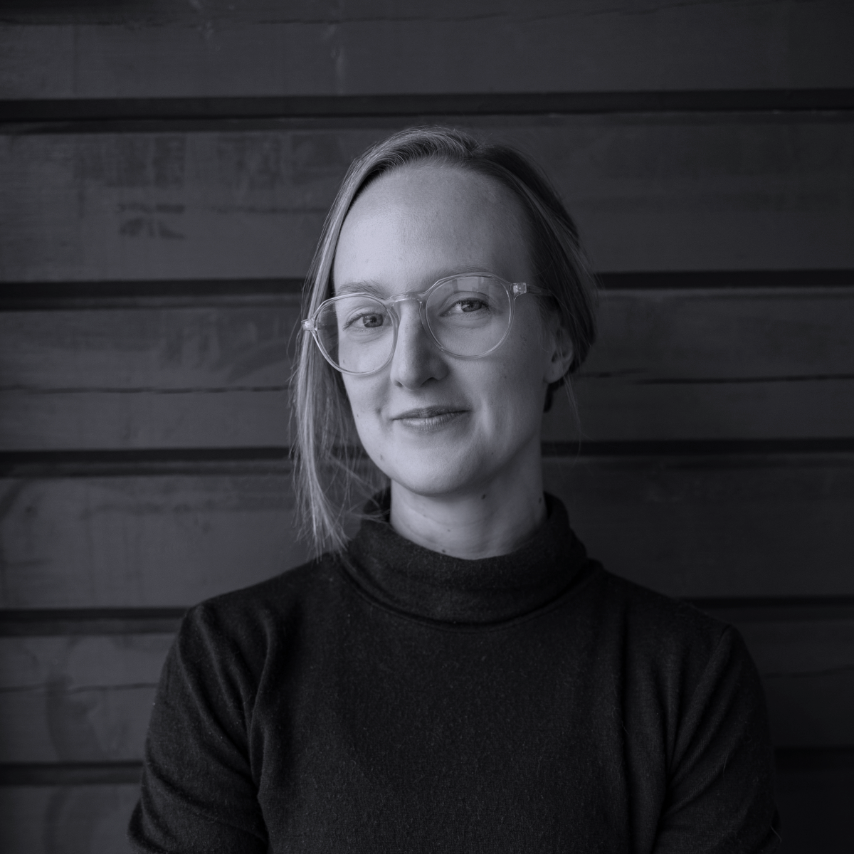 Mustavalkoinen valokuva Teasta, jolla on poolopaita ja silmälasit ja hiukset kiinni. Tea hymyilee hieman sivuttain kameralle.