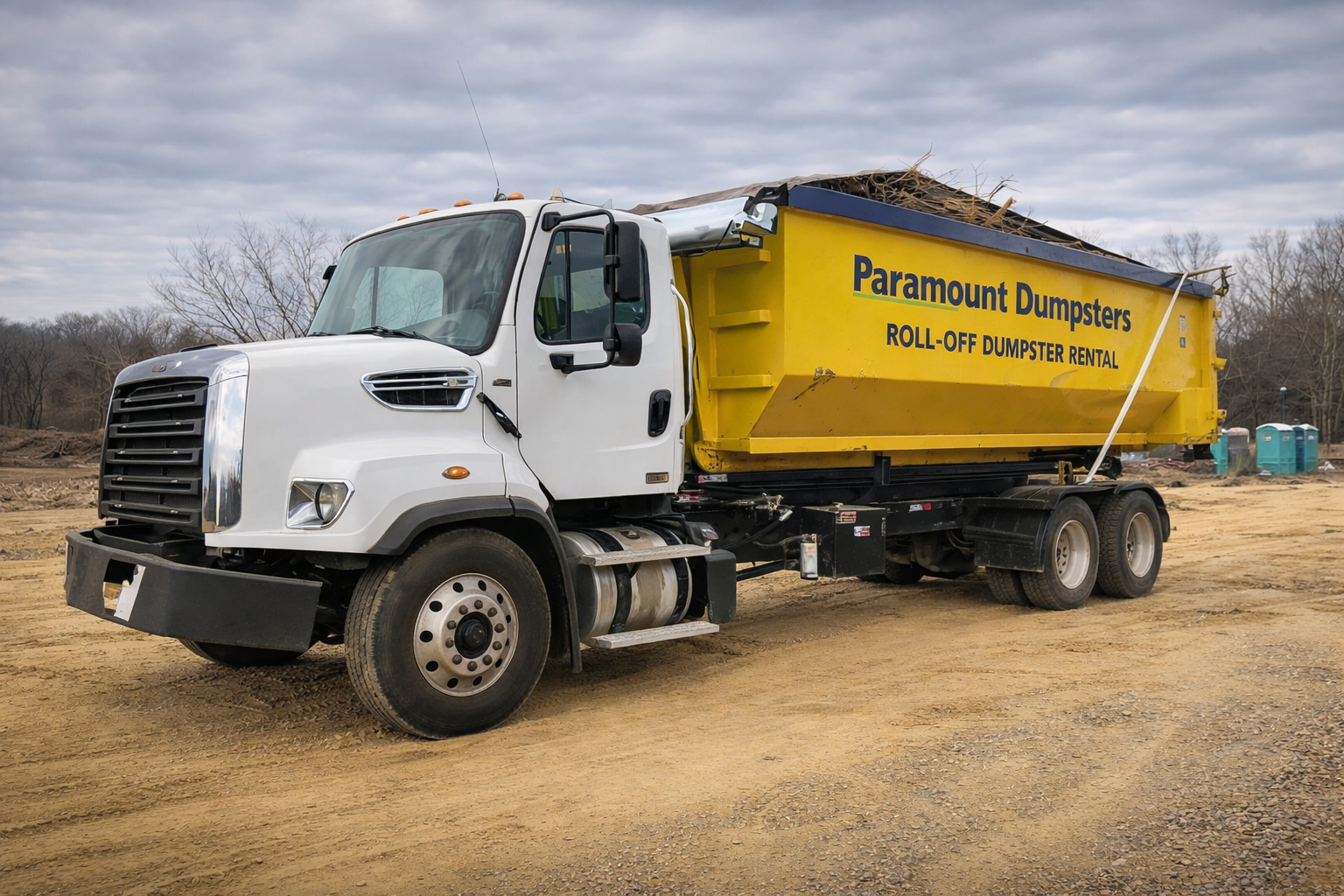 On Hernando, MS Construction Job having away construction debris in our dumpster. A white and yellow dump truck on a construction site, with a yellow container labeled "Paramount Dumpsters Roll-Off Dumpster Rental."