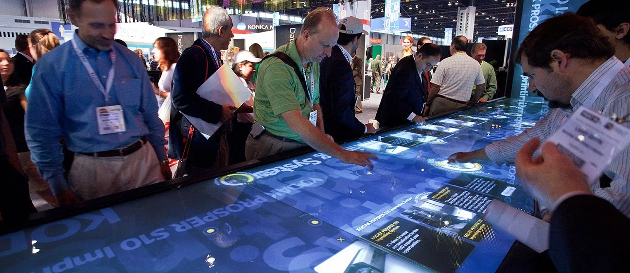 Interactive touchscreen table with people interacting with information on Kodak's pipeline of printer products