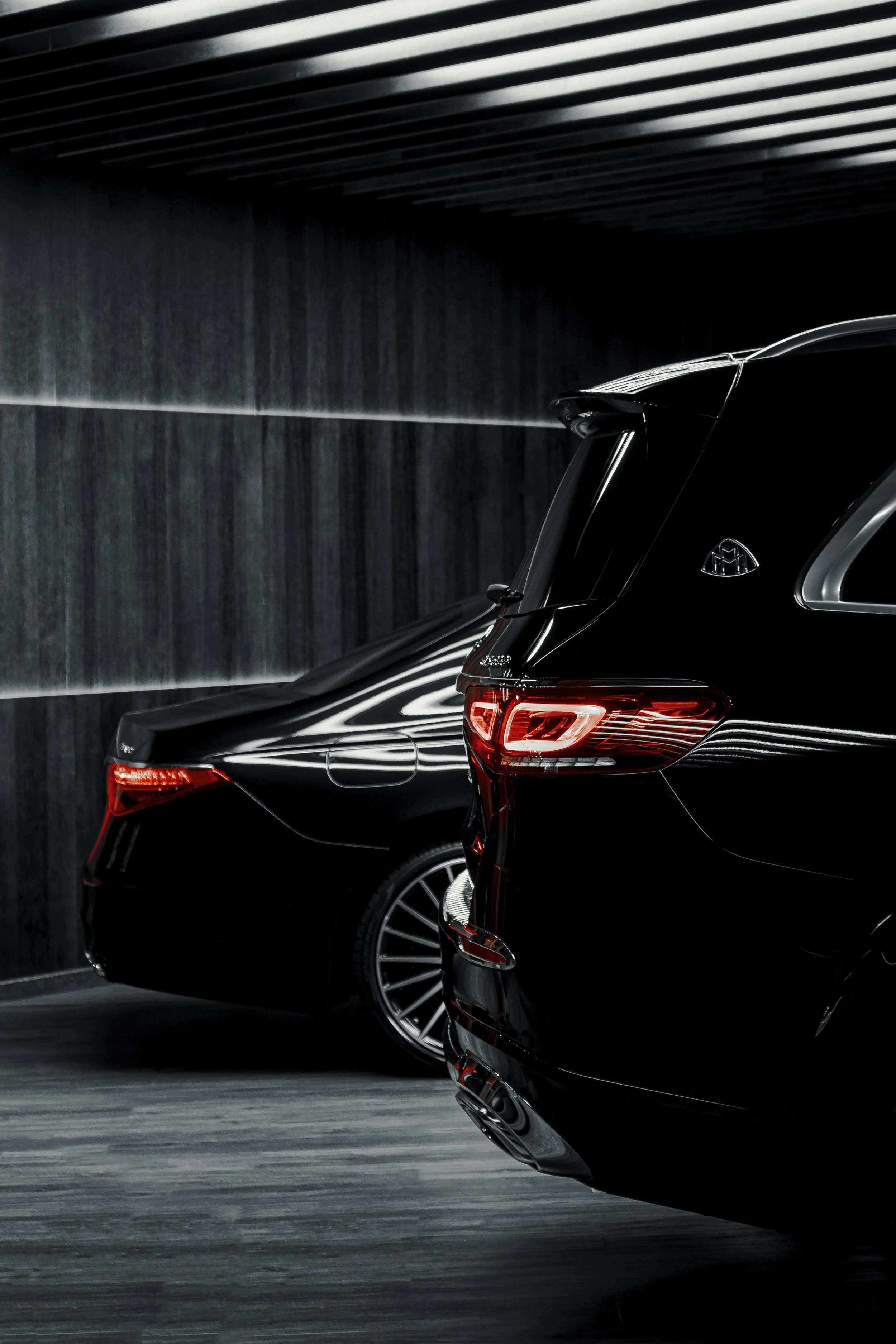 Close-up of black luxury cars with shiny surfaces, parked indoors with a dark, modern interior and horizontal lighting.