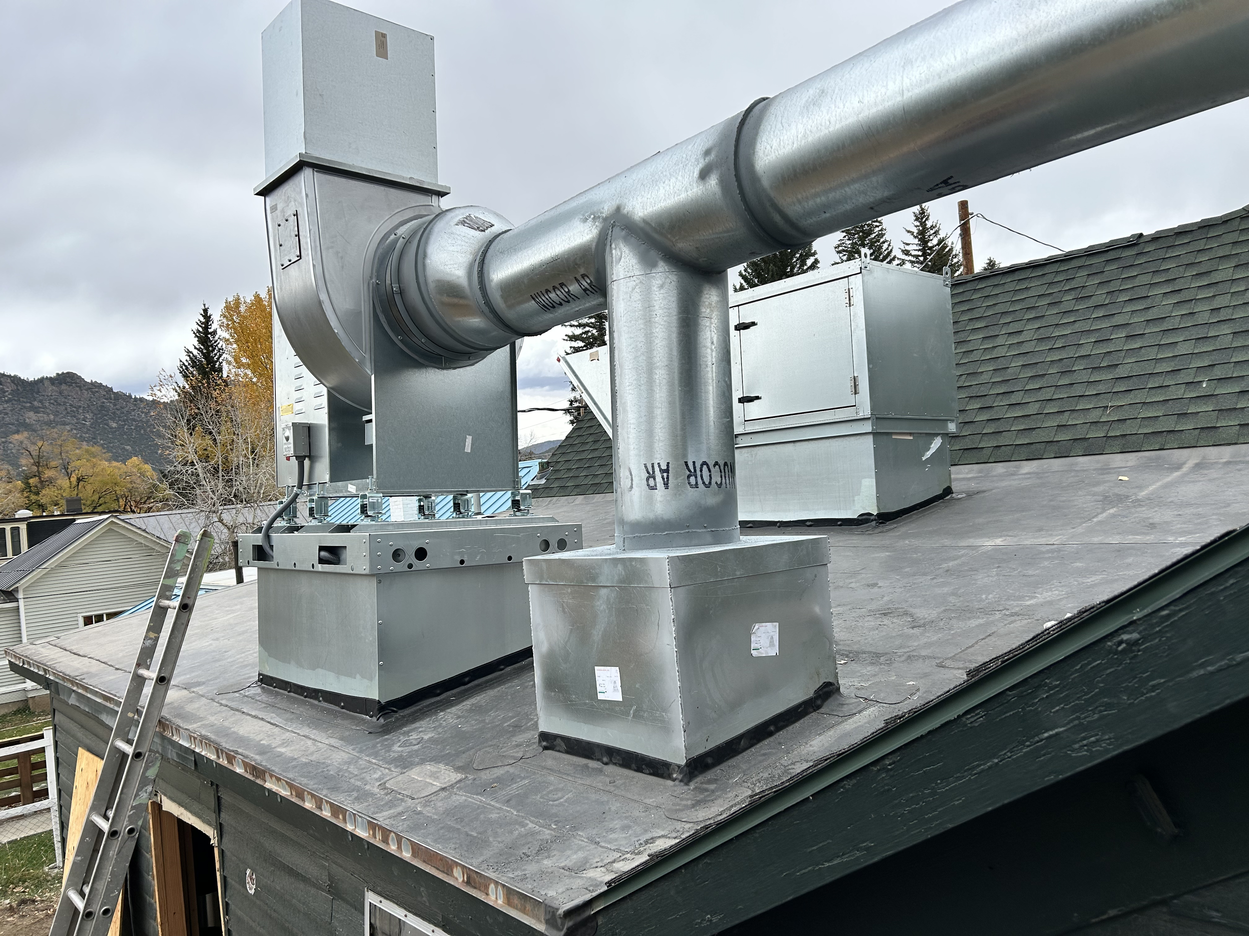 Metal HVAC vent system installed on a rooftop with surrounding houses and mountains in the background.