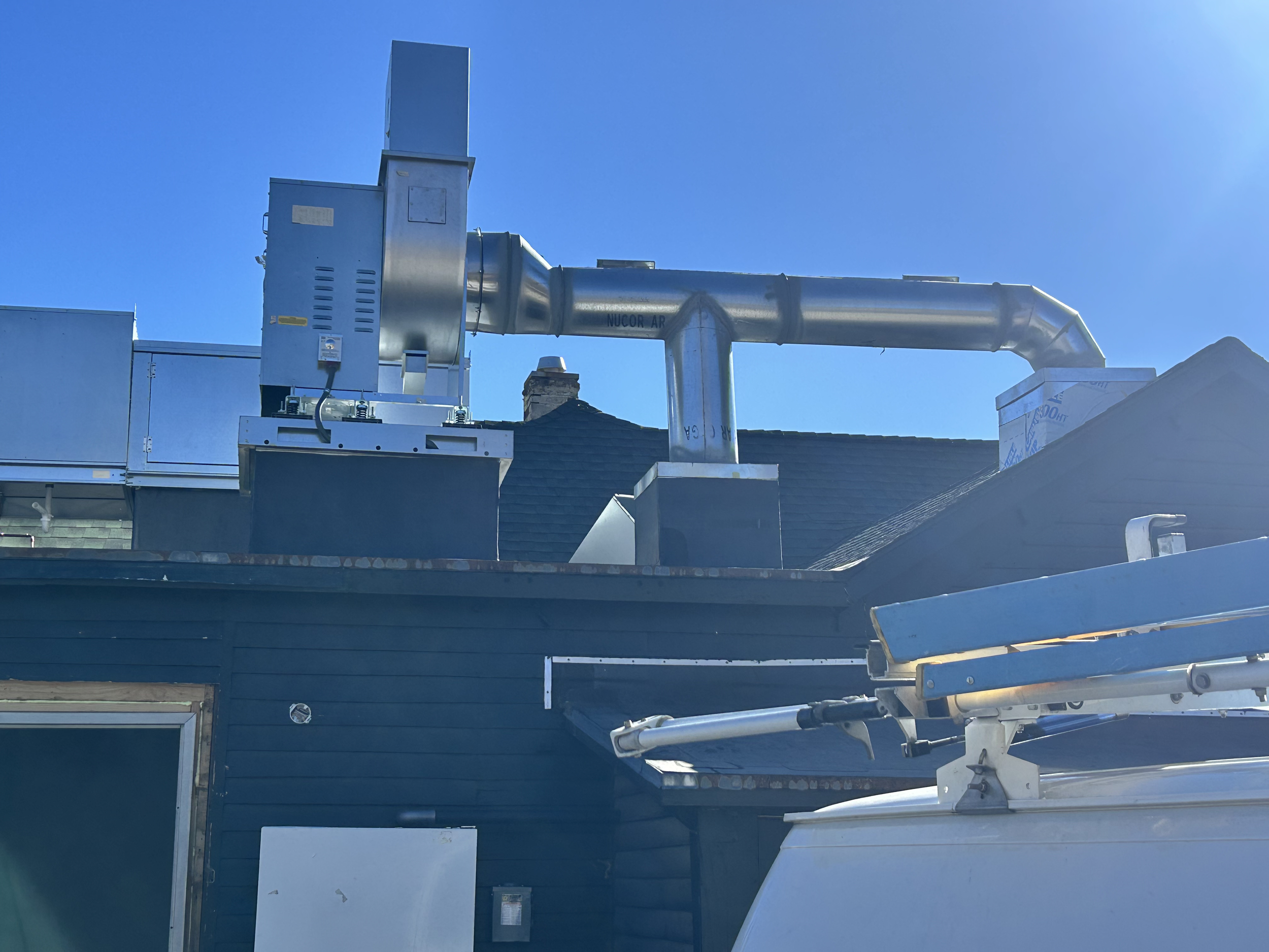 Rooftop with HVAC system and ductwork under a clear blue sky.