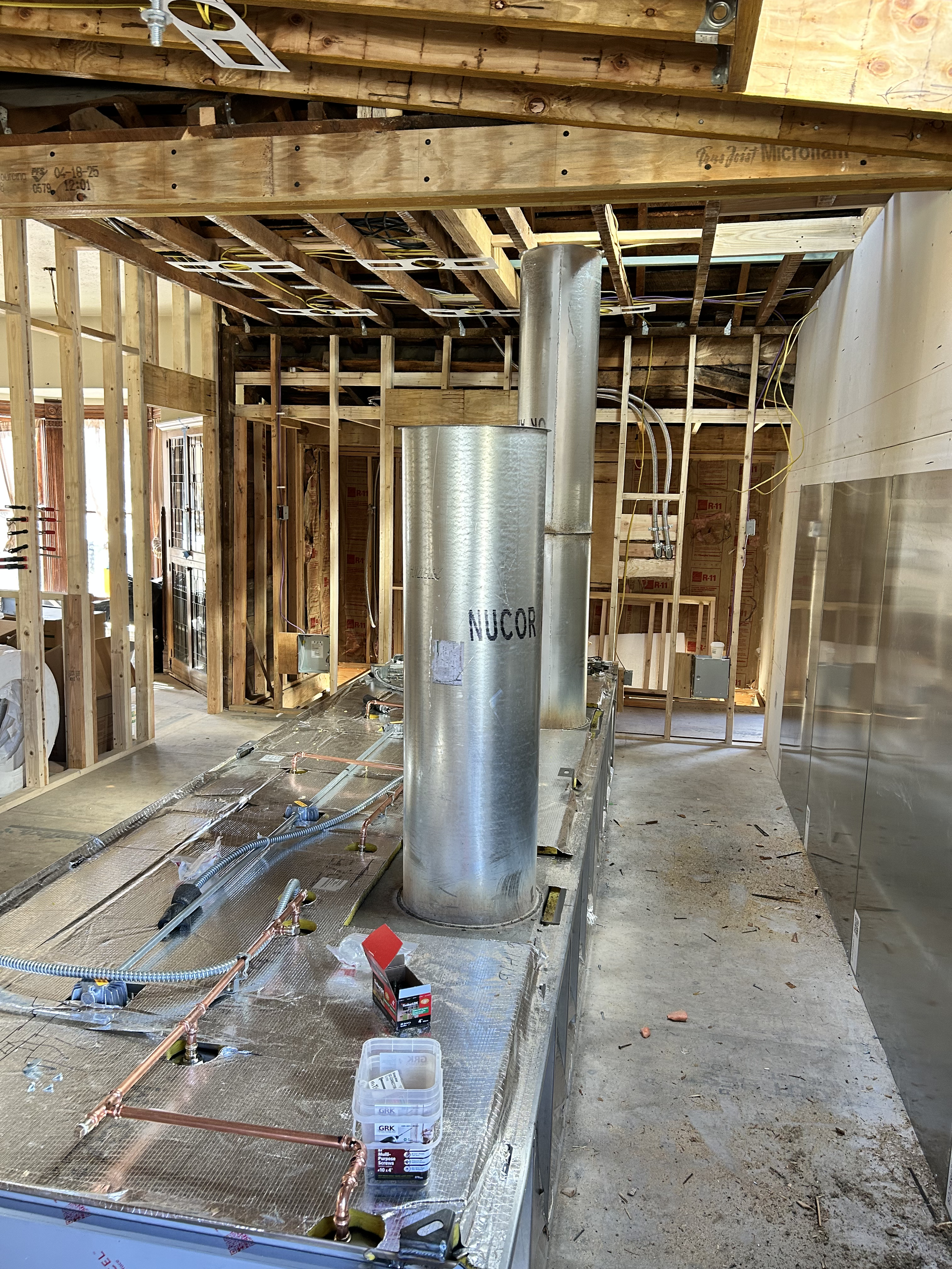Construction site showing an unfinished kitchen with exposed wooden framing, wiring, and ductwork, and metal HVAC components installed.