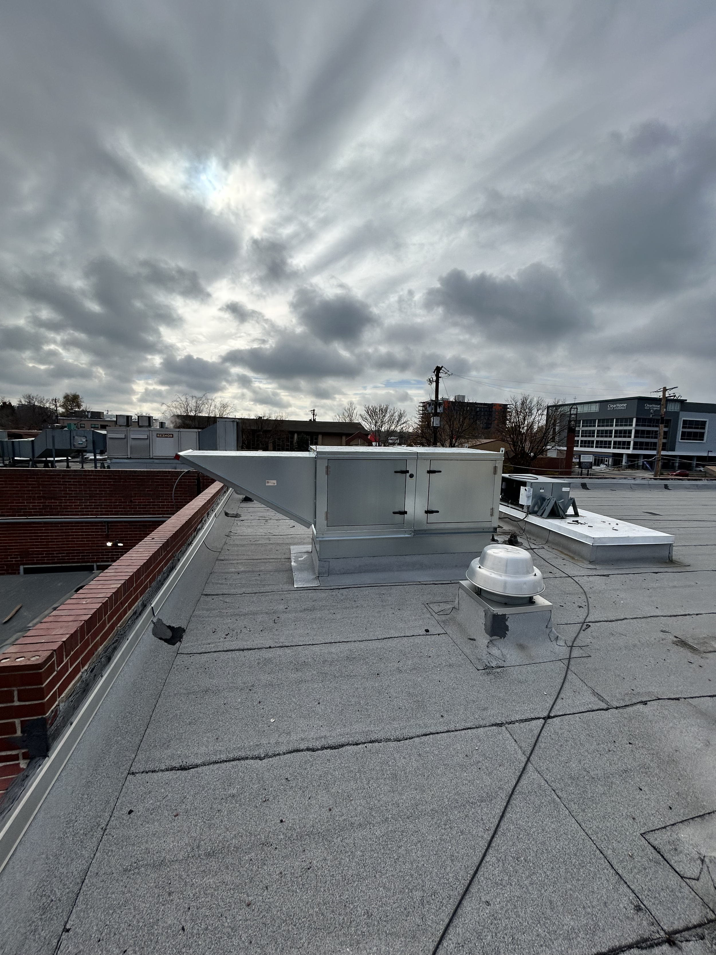 Rooftop view with HVAC units, vents, and a cloudy sky in the background.