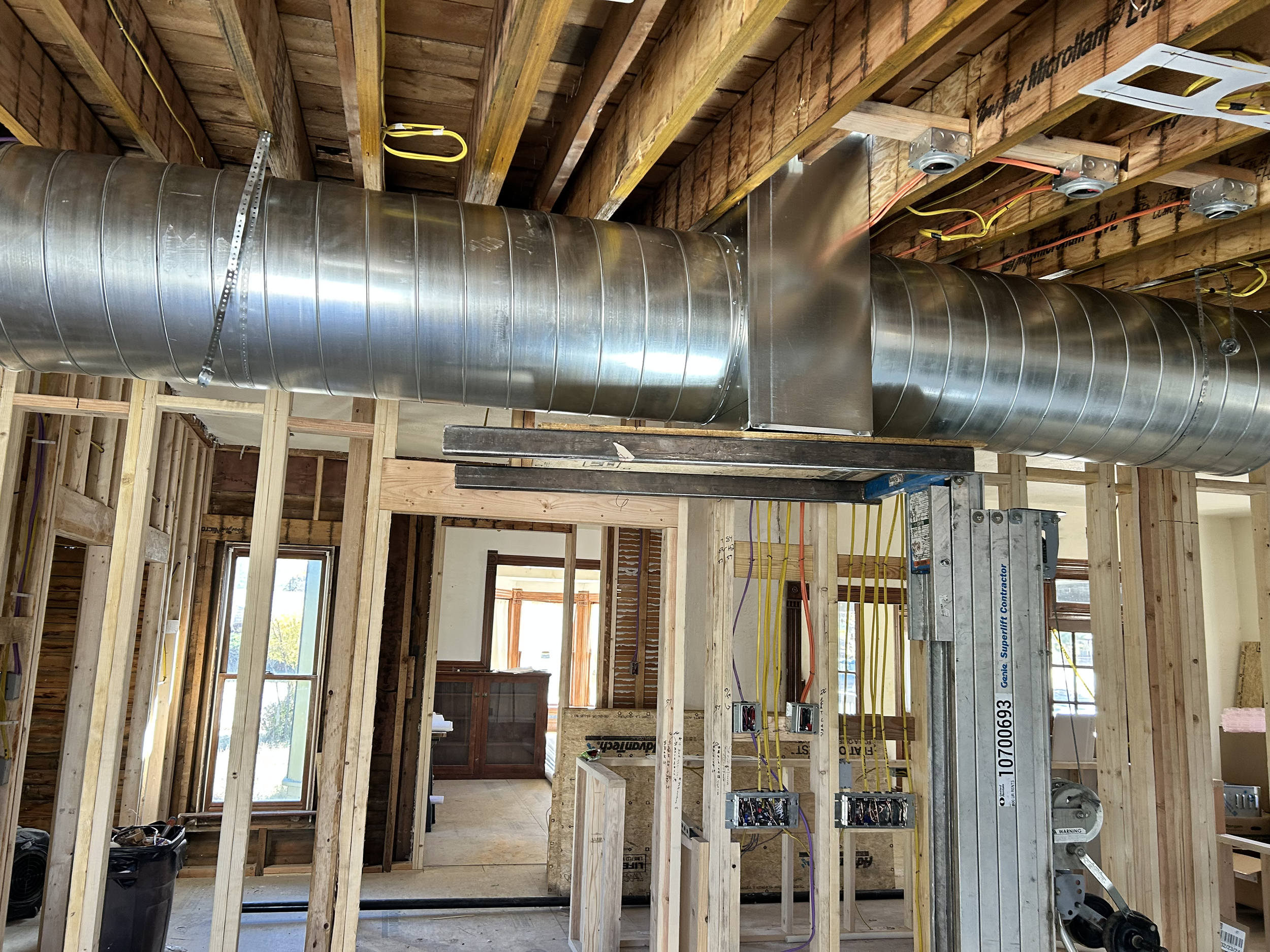 Construction site with exposed wooden framing, a large metal duct, yellow electrical wires, and open wall spaces.