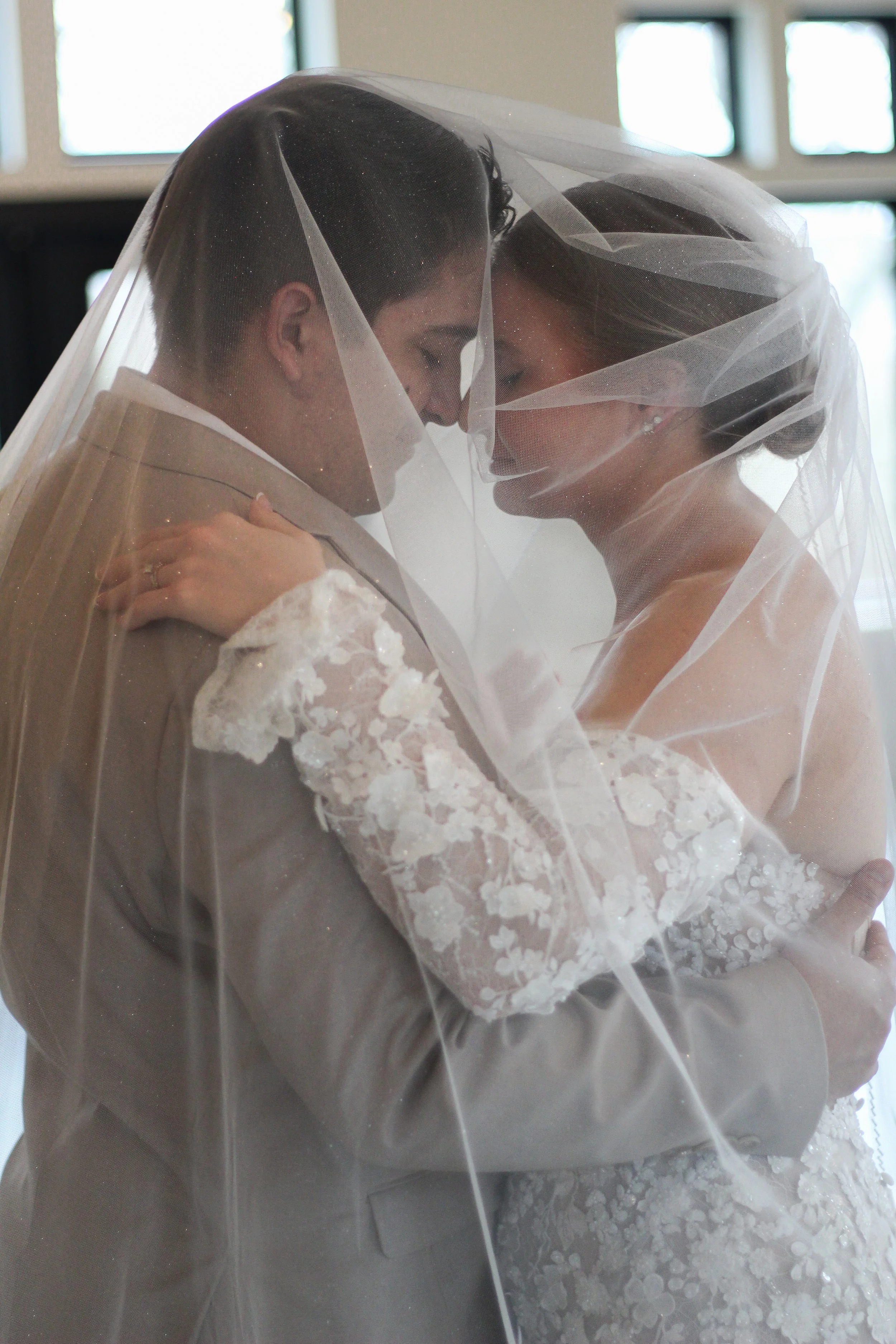 A bride and groom embrace under a bridal veil at their wedding ceremony.