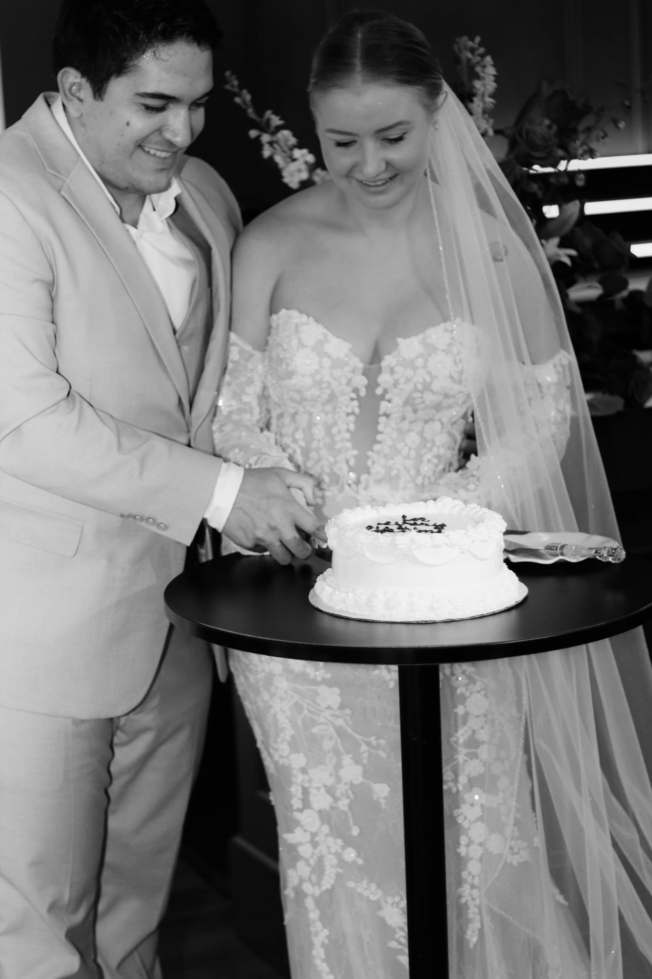 A bride and groom in wedding attire cutting a wedding cake together at a celebration.