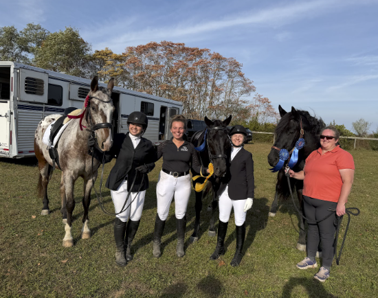 Professional horse trainer Emma Davern with a show clients. Four women and two horses standing outdoors with a horse trailer in the background, some holding the horses' reins.