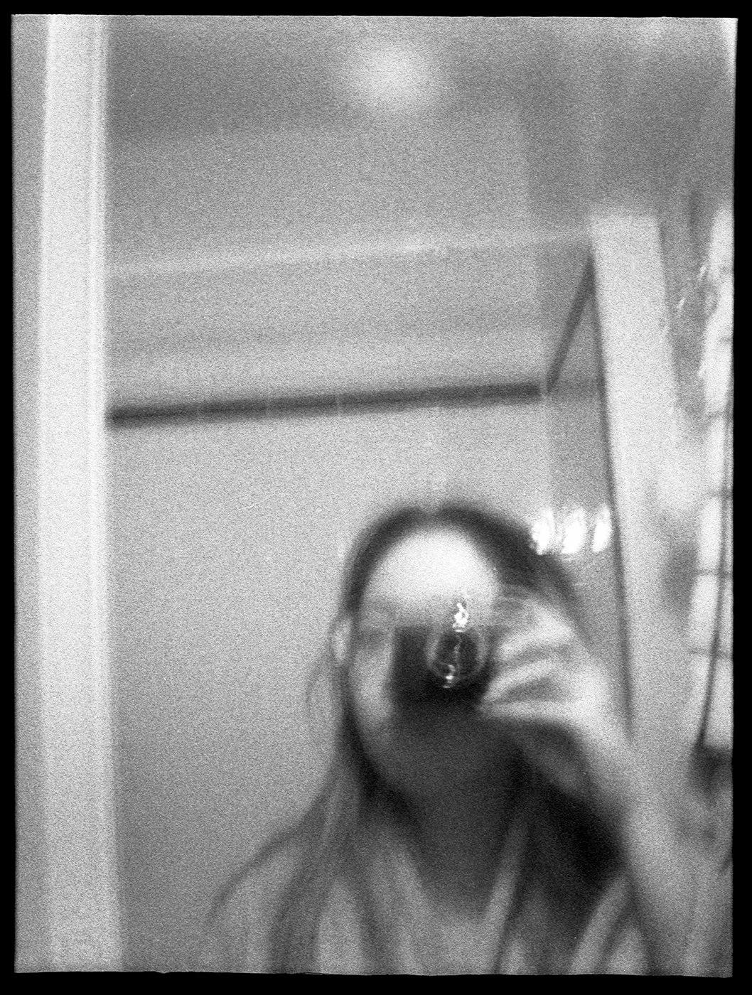Black and white photo of a person taking a mirror selfie in a bathroom or bedroom, with hair covering part of the face.