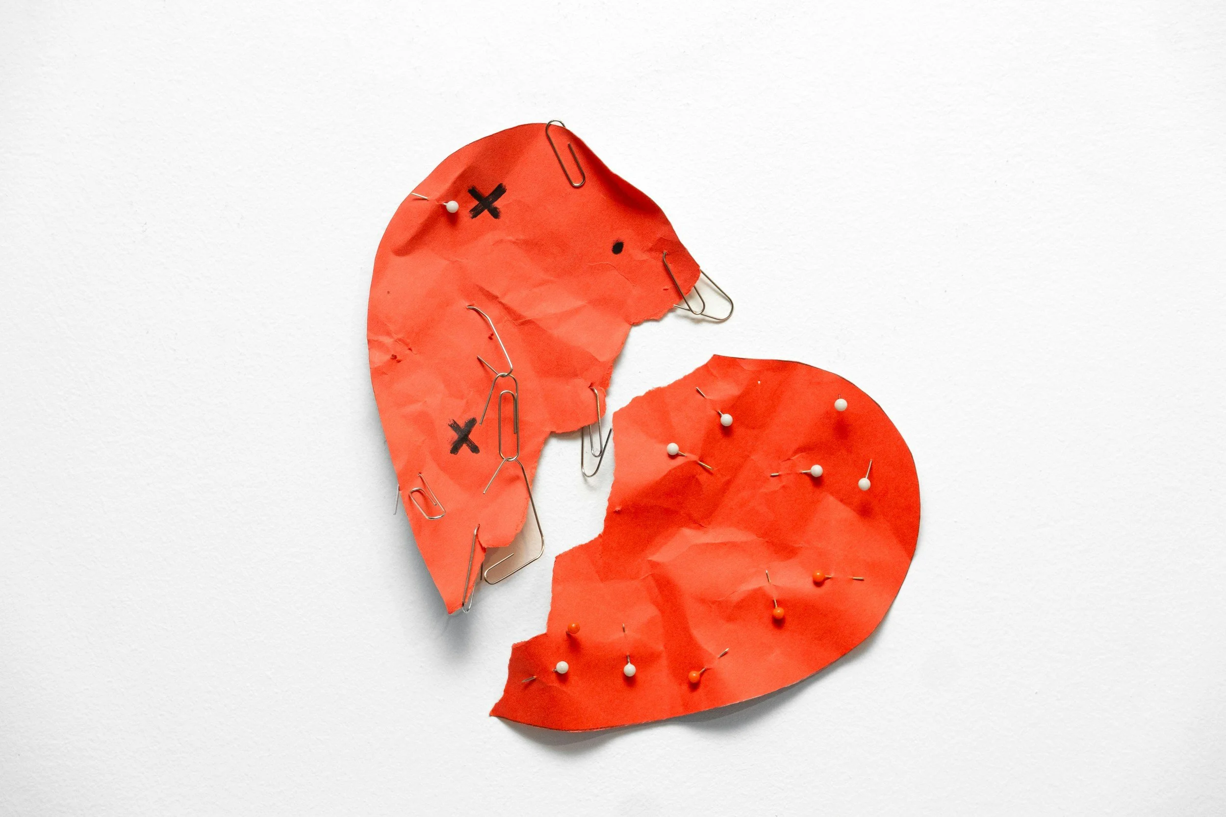 A cardboard heart torn in two pieces with pins stuck in it