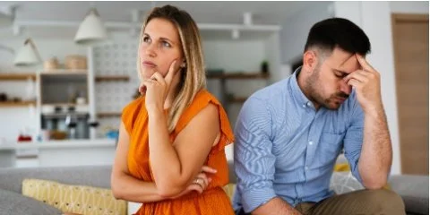A man and woman sit back to back, both unhappy
