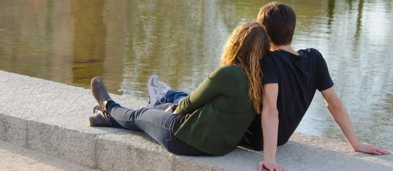 Couple sits looking at body of water