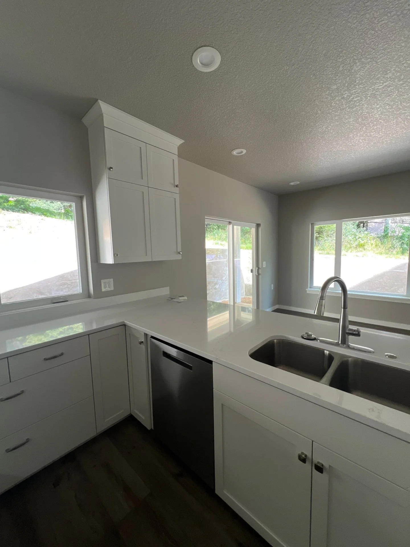A modern kitchen with white cabinets, a double sink, and large windows allowing natural light.