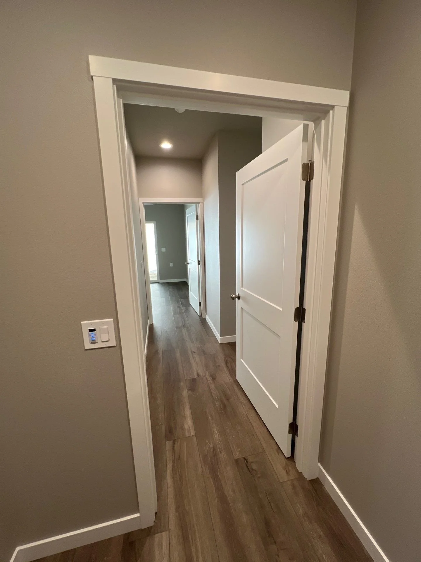 A hallway with wooden flooring, gray walls, white trim, and an open white door leading to other rooms.