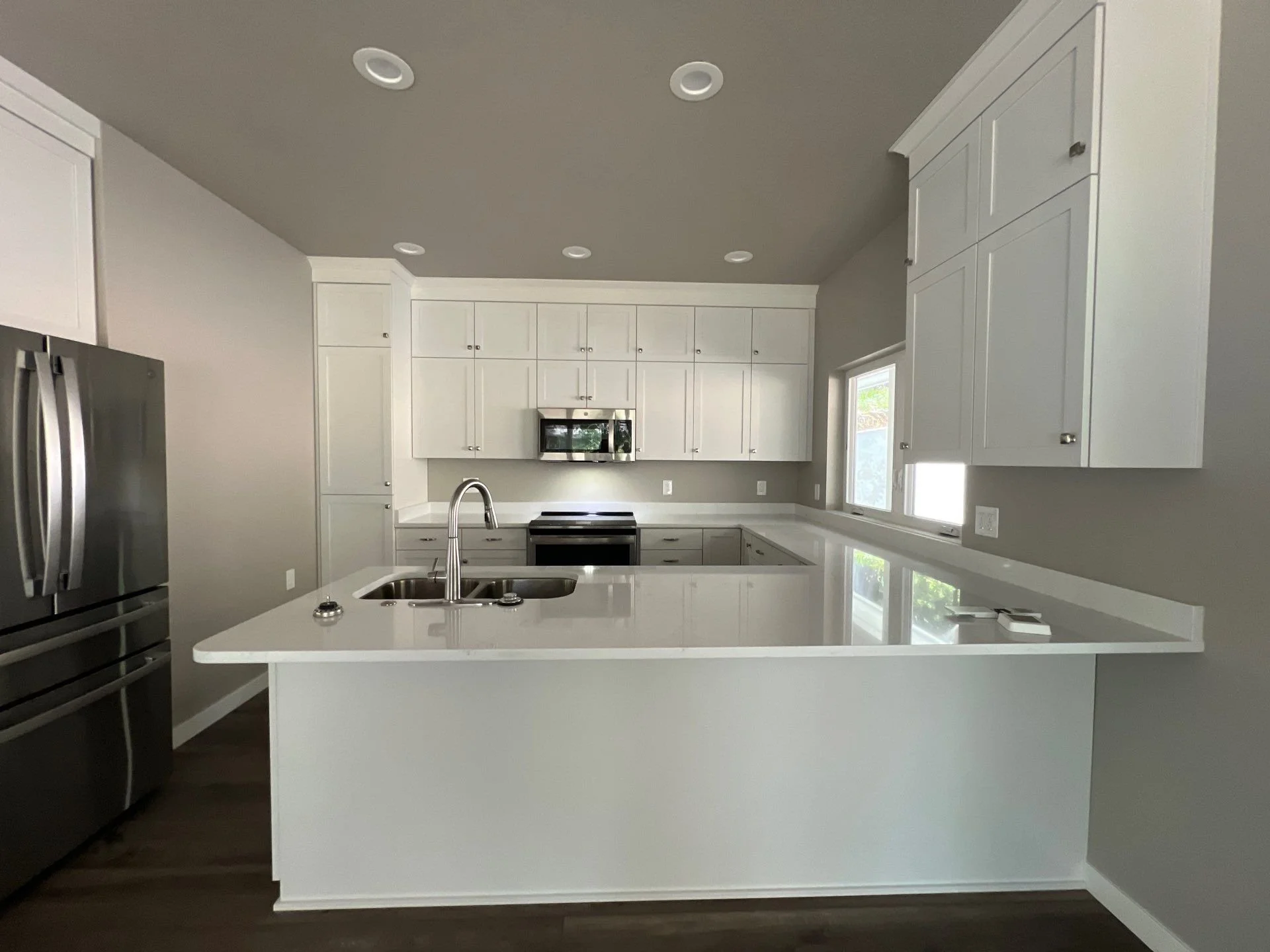 Modern kitchen with white cabinets, a large island with a sink, stainless steel refrigerator, oven, microwave, and windows.