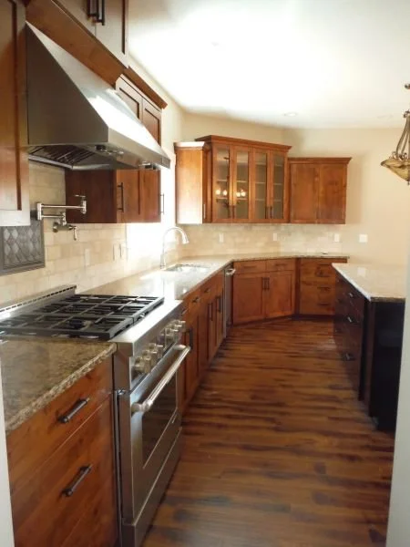 Kitchen with wooden cabinets, a stainless steel stove and hood, granite countertops, and hardwood flooring.