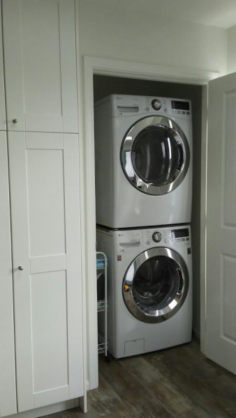 White stacked washer and dryer in a laundry closet next to white cabinets.