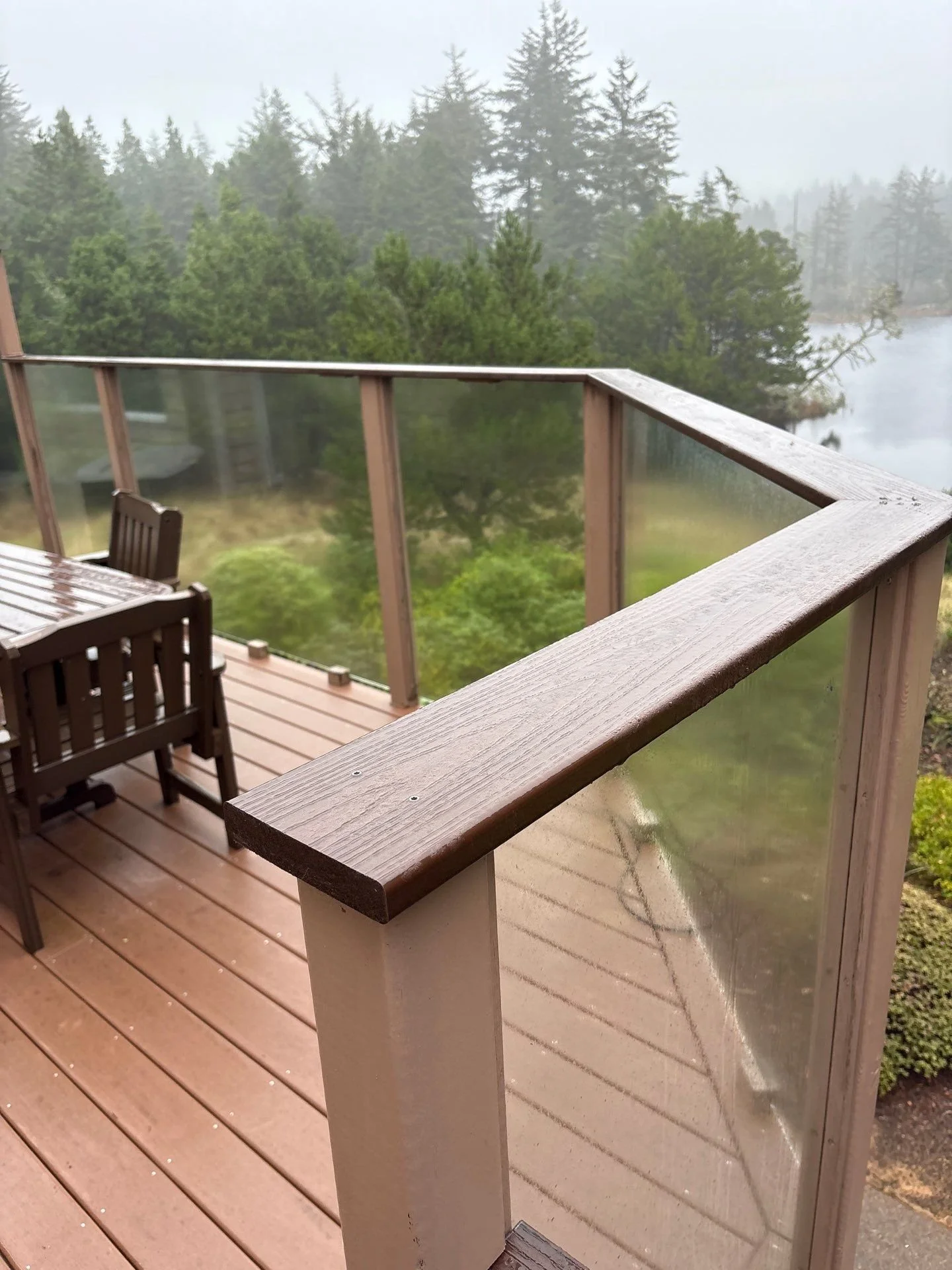 Wooden deck with outdoor furniture, overlooking a foggy forested lake view, surrounded by tall trees.