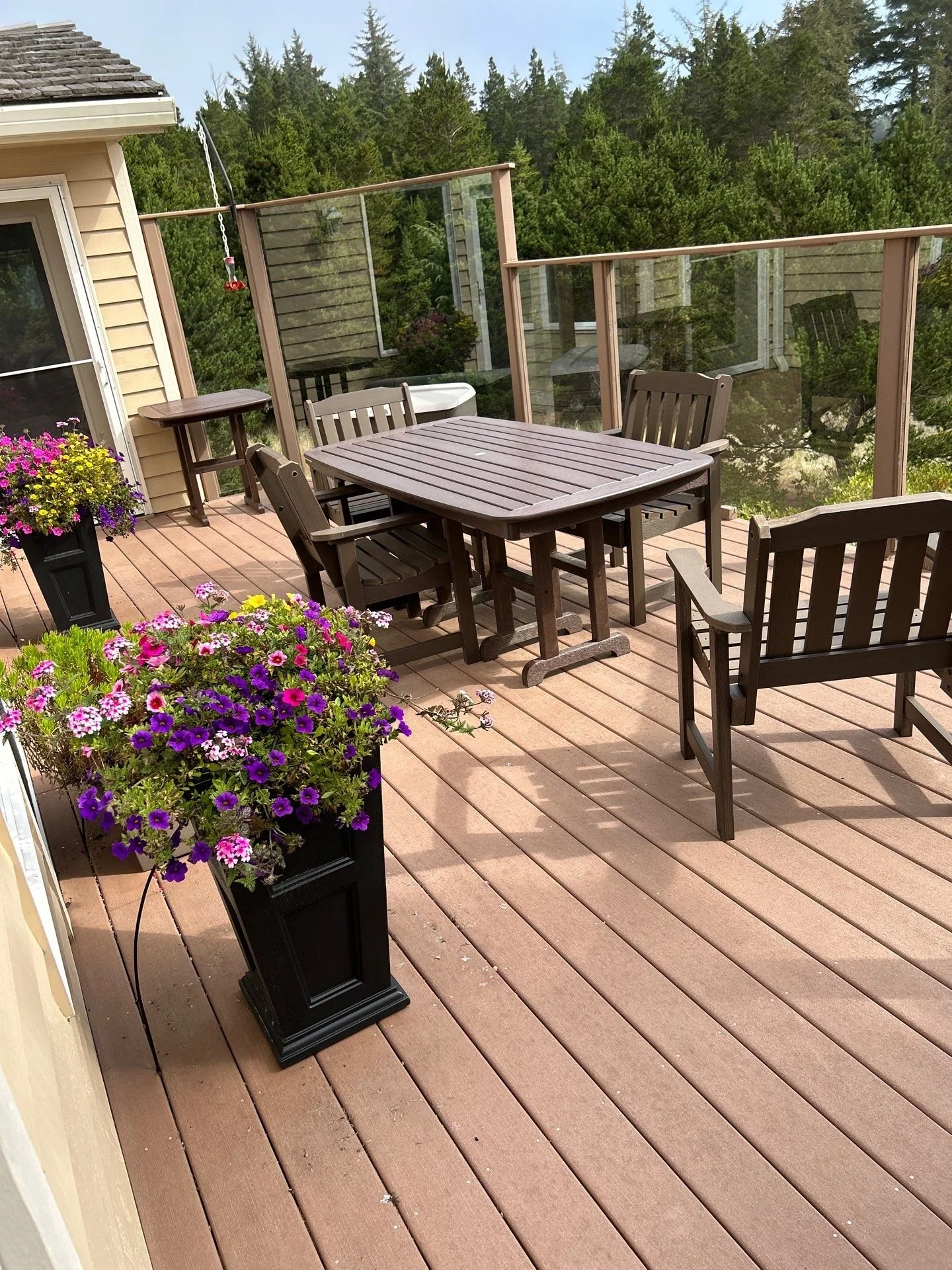 Wooden outdoor balcony with patio furniture and potted flowers, surrounded by trees.