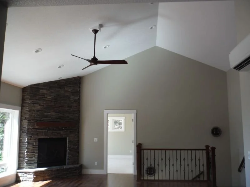 Living room with a high vaulted ceiling, ceiling fan, stone fireplace, and a staircase with wooden railing.