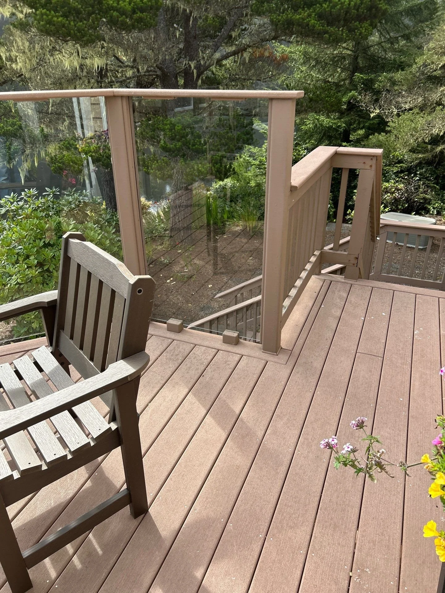 Wooden outdoor deck with railing, stairs, and a wooden chair, surrounded by greenery and trees.