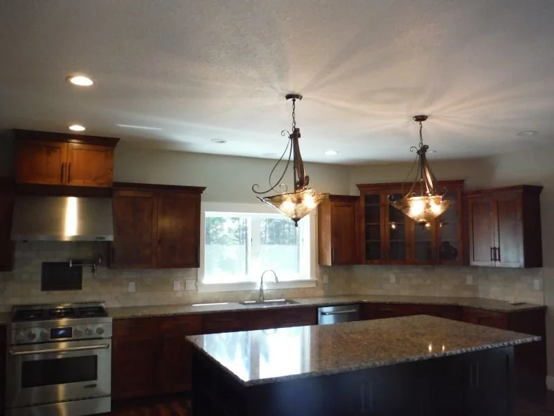 Modern kitchen with wooden cabinets, a granite island, stainless steel appliances, and pendant lighting fixtures.