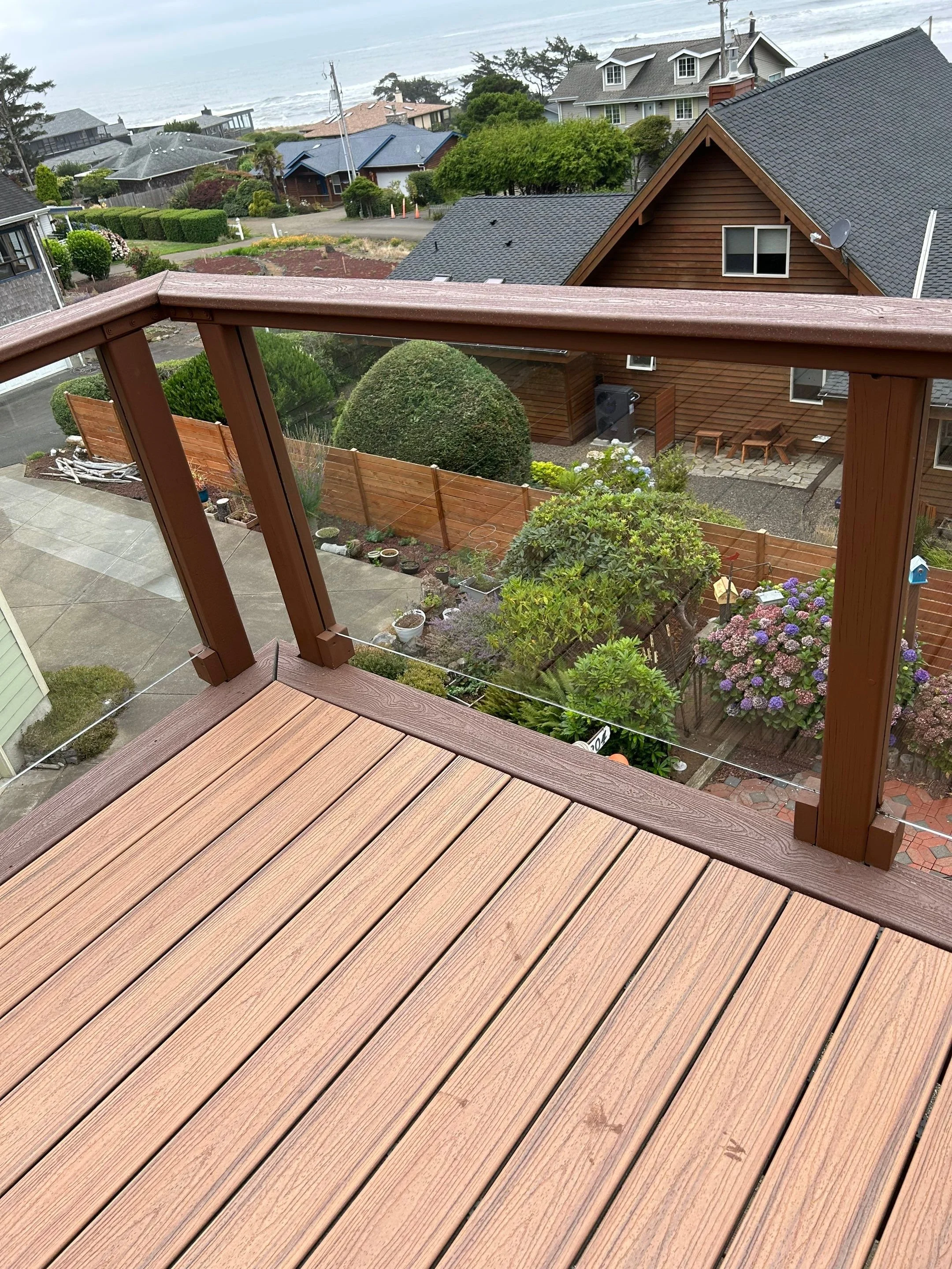 View from a wooden balcony overlooking a residential neighborhood, coastline, and ocean in the distance, with cloudy weather.