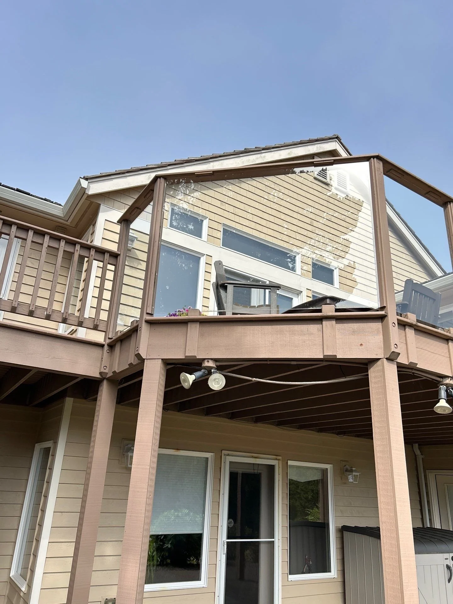 Backyard view of the house with a two-story deck, featuring a glass railing on the upper deck, patio furniture, and a partially covered lower deck with sliding glass doors.