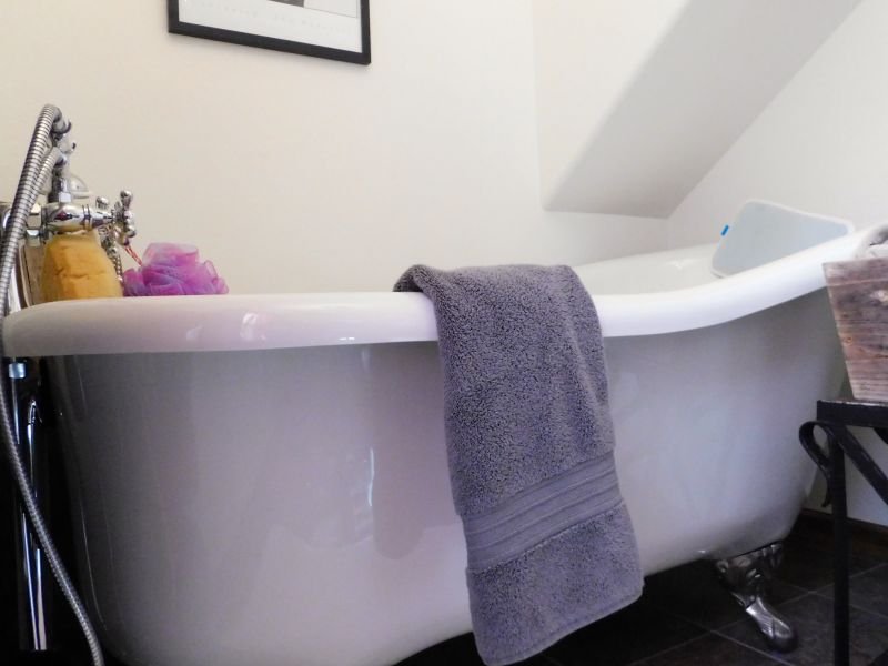 Clawfoot bathtub in a bathroom with a gray towel hanging over the side, with bath products and a picture frame on the wall.