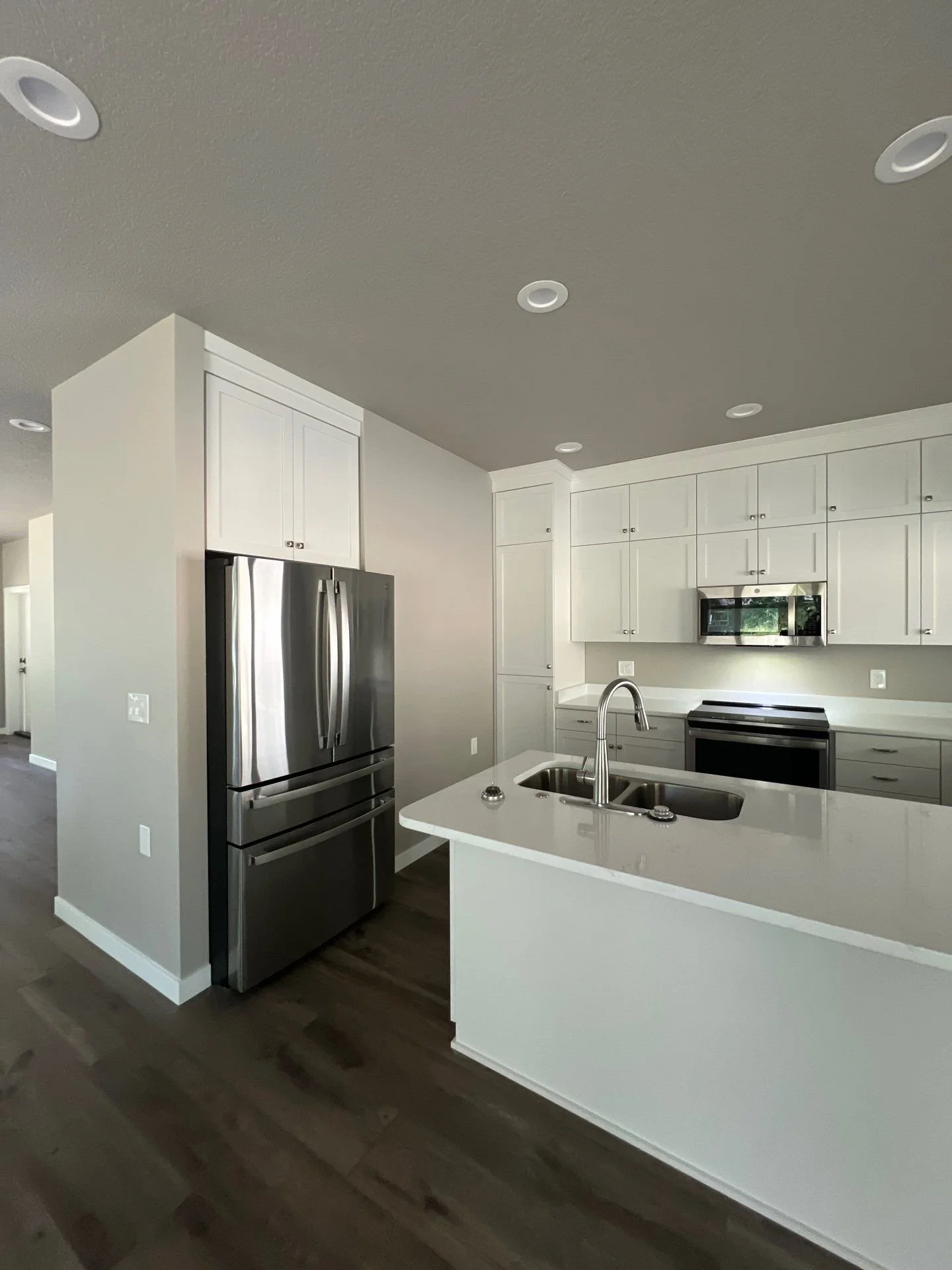 Modern kitchen with white cabinets, stainless steel refrigerator, microwave, oven, and a white kitchen island with a double sink.