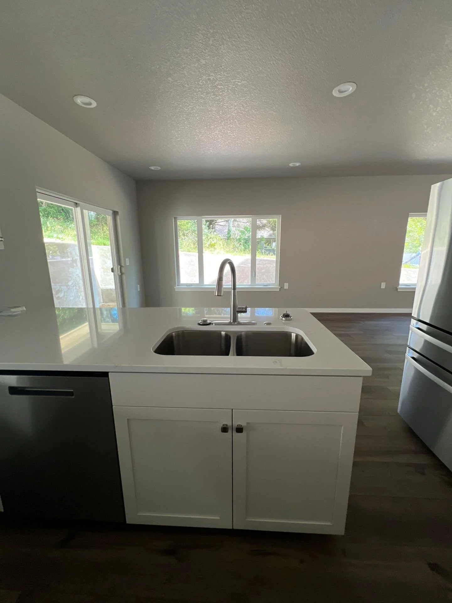 Modern kitchen with white cabinets, stainless steel sink, and open layout with large windows and sliding glass door.
