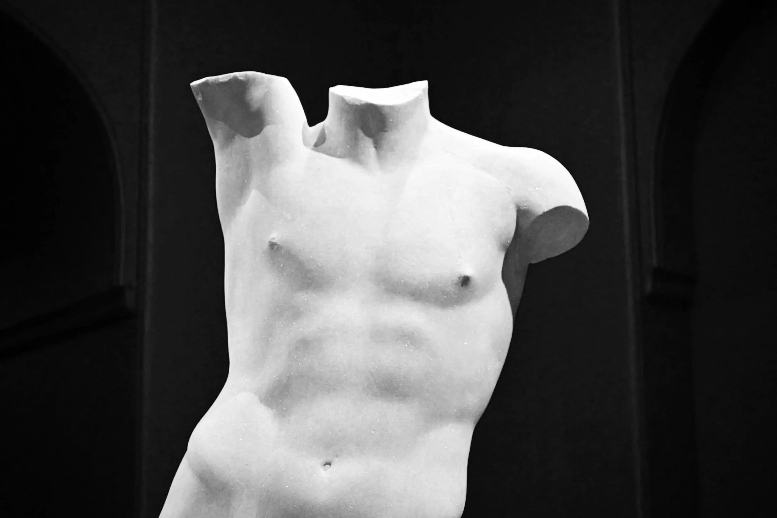 Close-up of a white marble sculpture of a male torso without a head or arms, displayed in a museum.