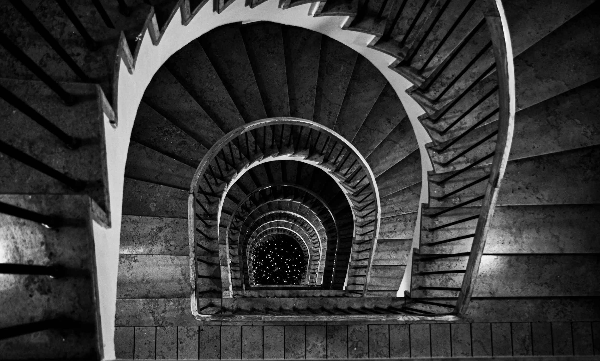 Black and white image of a spiral staircase viewed from above, winding downward with a dark center.