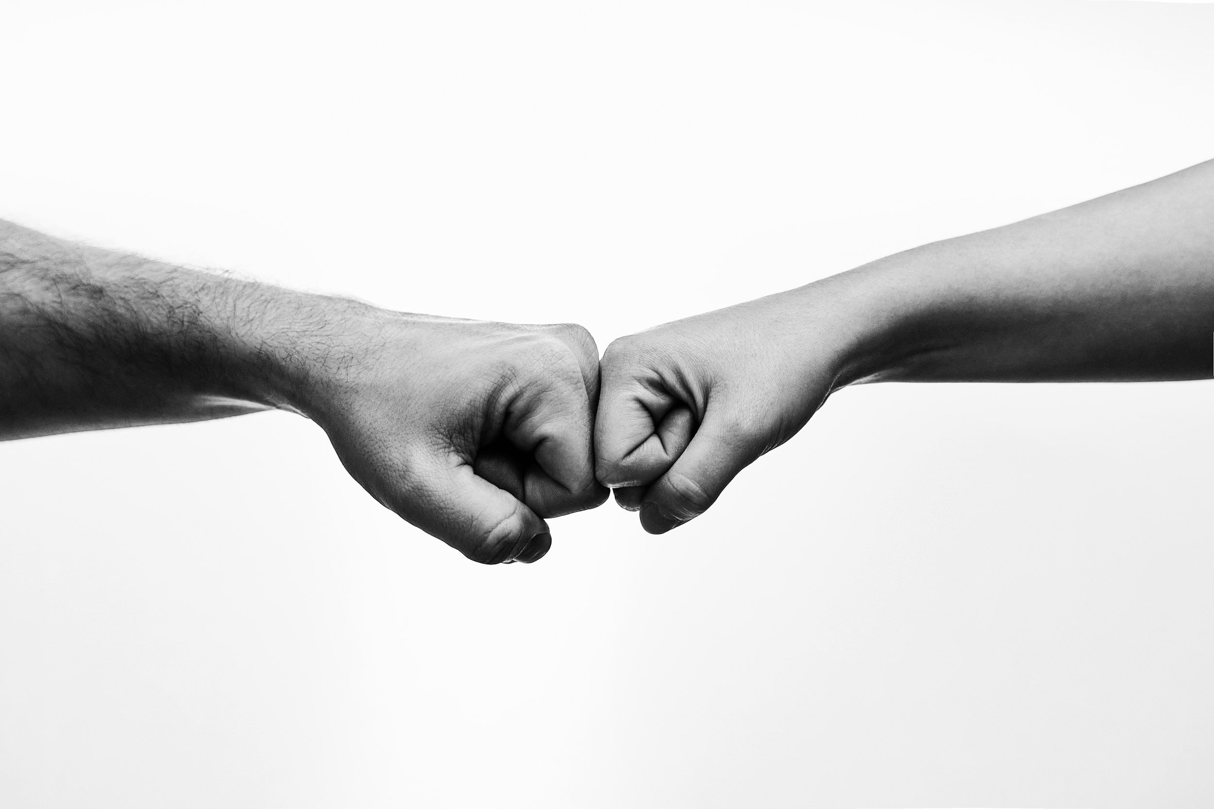 Two hands, one with darker skin and one with lighter skin, engaging in a fist bump against a plain white background.